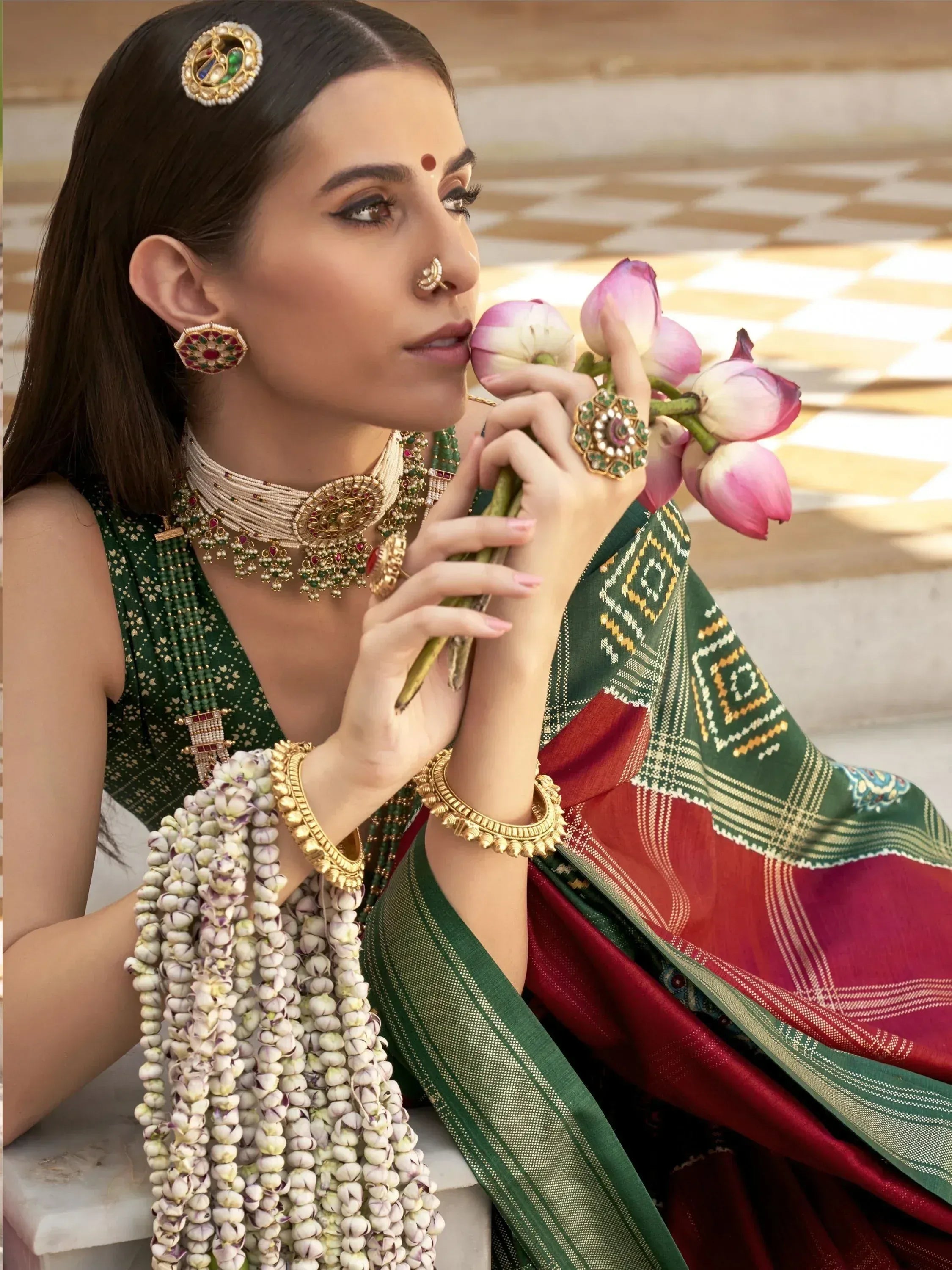 Woman in green and red ethnic saree with traditional jewelry holding lotus flowers