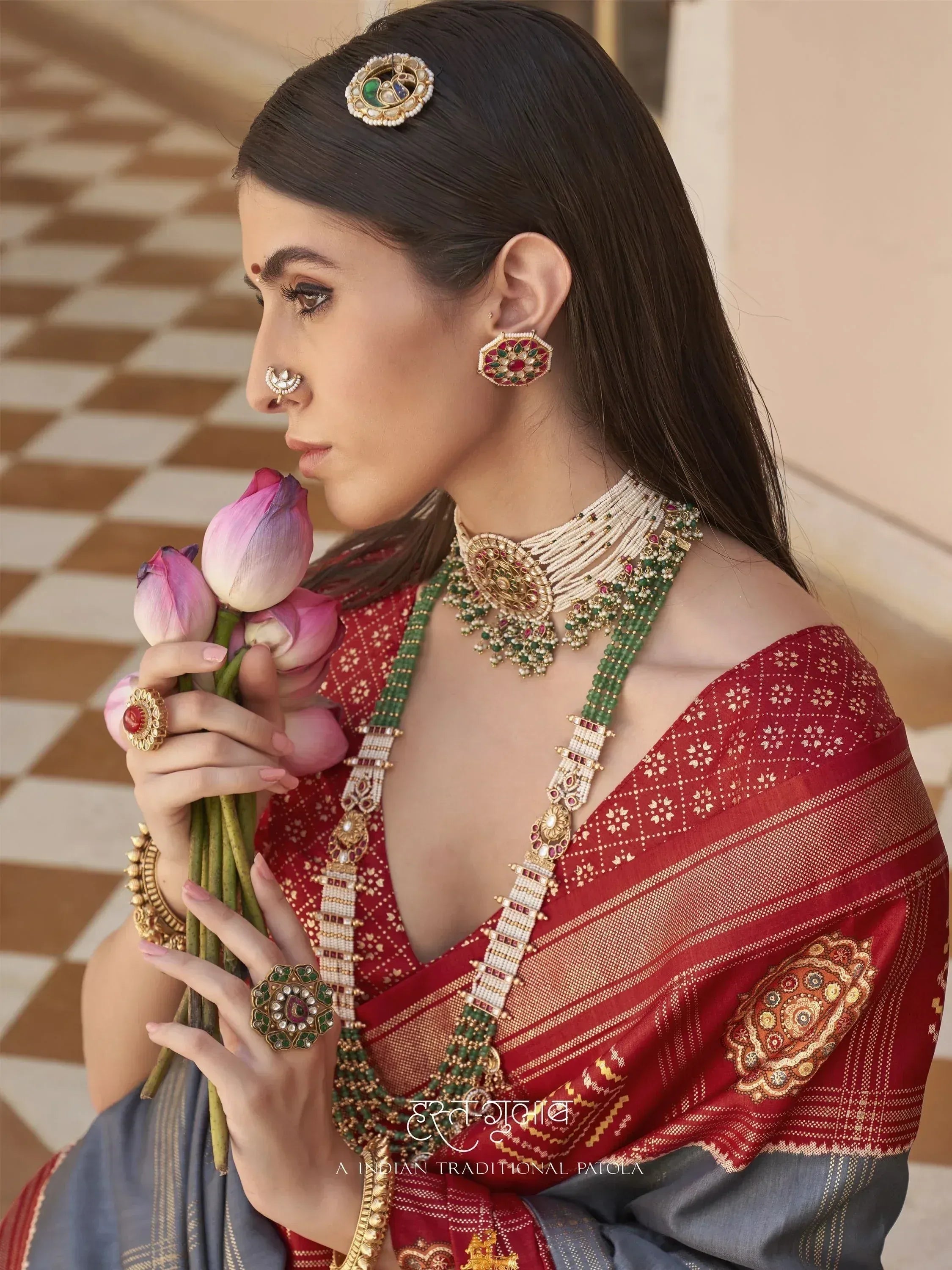 Woman in red and grey Indian saree with traditional jewelry holding lotus flowers