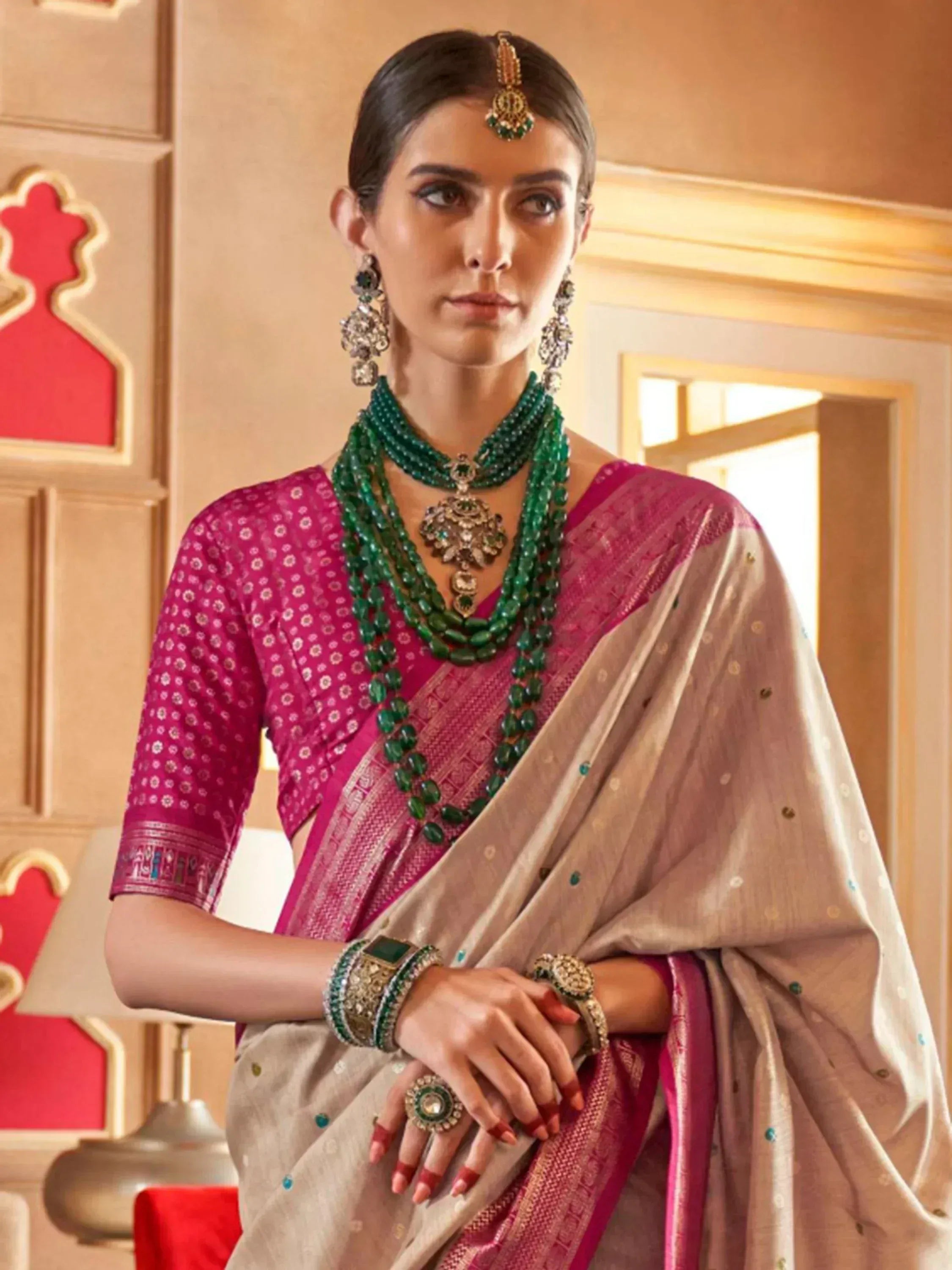 Woman in elegant pink and beige saree with green jewelry, showcasing traditional Indian ethnic wear.