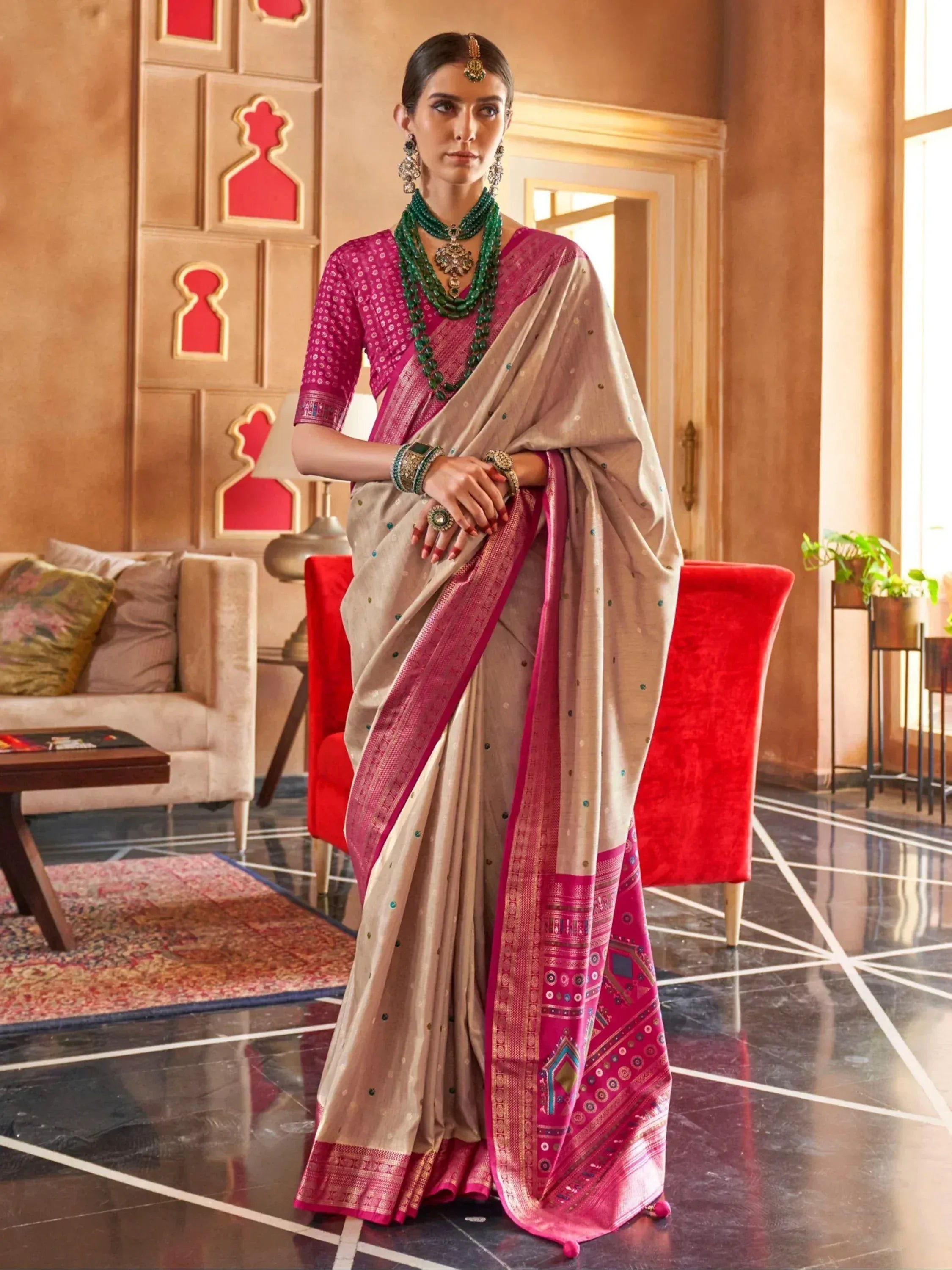 Elegant woman in beige and pink designer saree with intricate border, paired with green jewelry for ethnic occasions.
