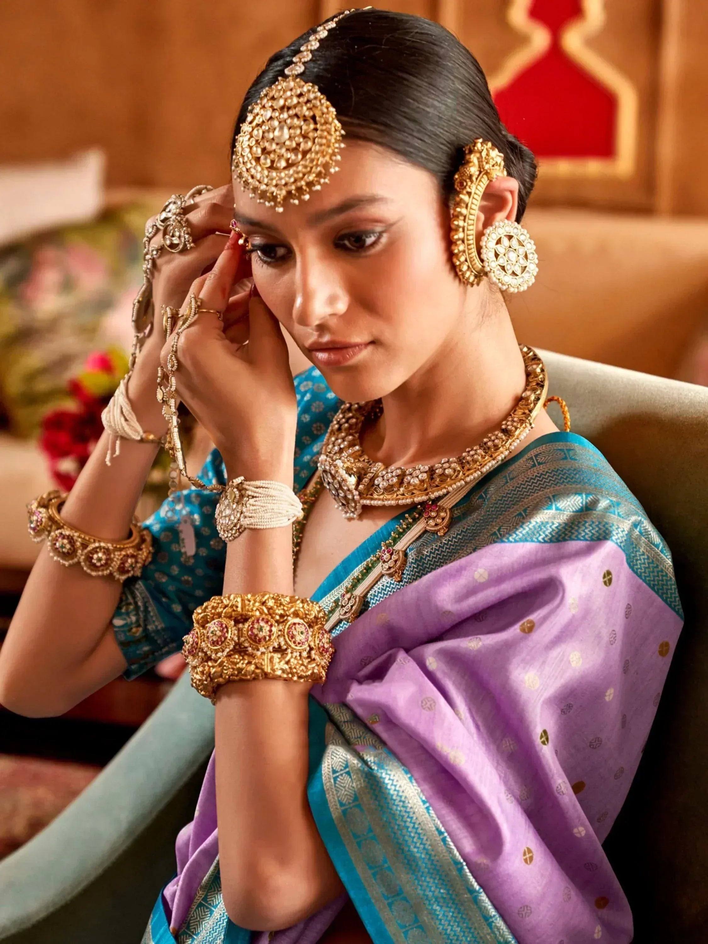 Woman in purple and blue saree with traditional Indian bridal jewelry, gold maang tikka, earrings, and bangles