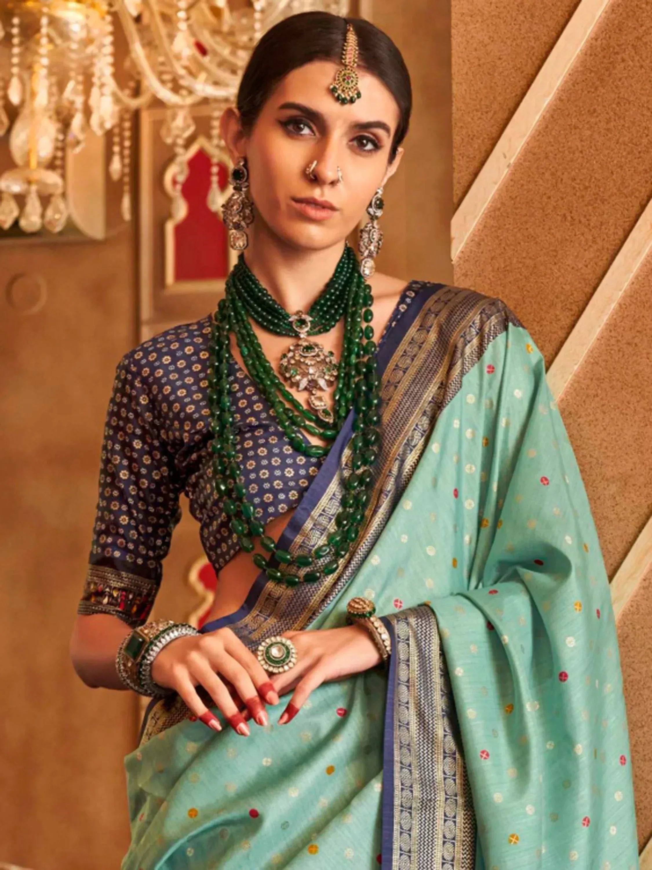 Elegant woman in mint green saree with blue blouse, traditional Indian jewelry, and ornate chandelier background