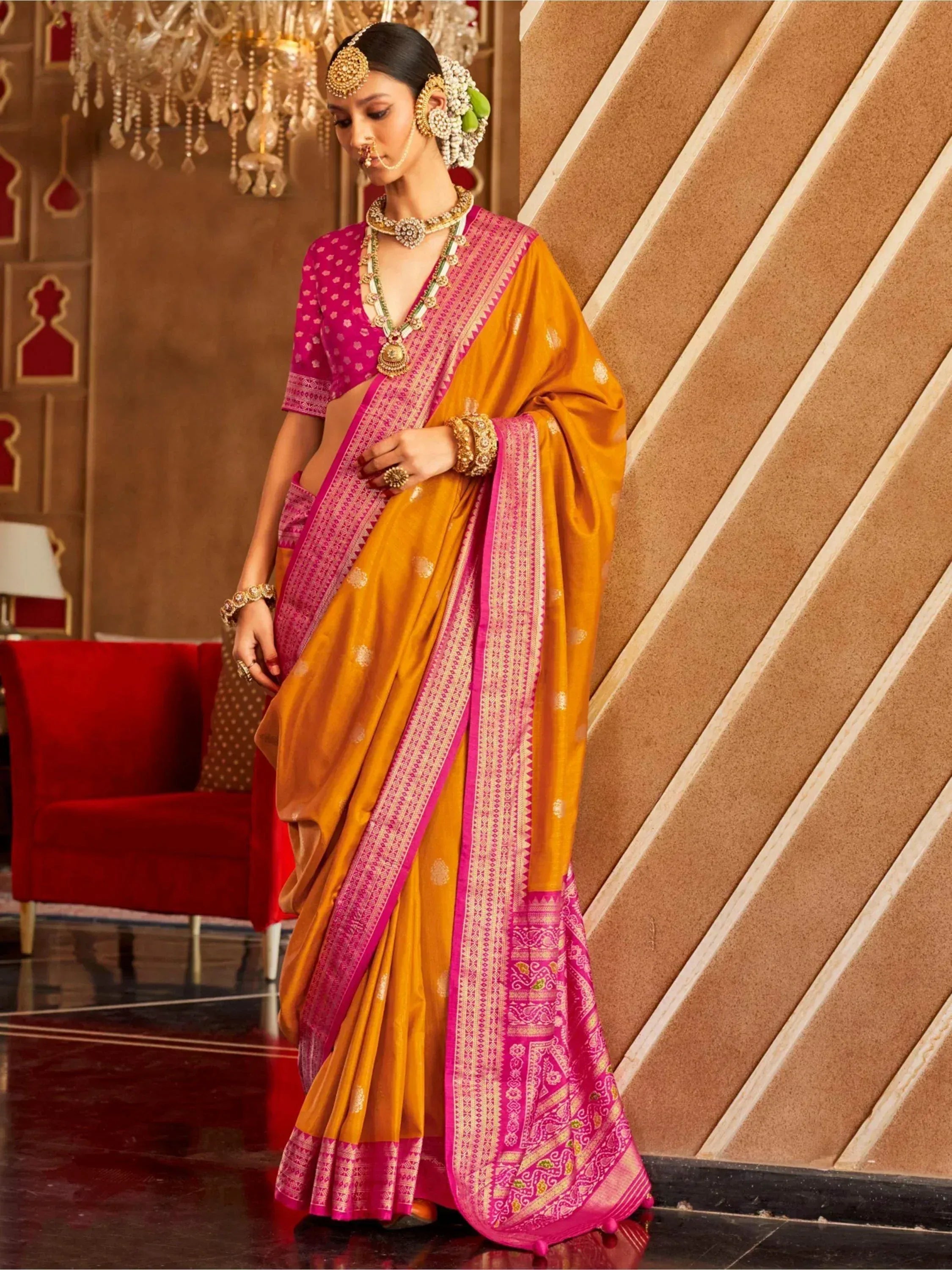 Woman in vibrant yellow and pink designer saree with intricate border, traditional jewelry, and floral hair accessory