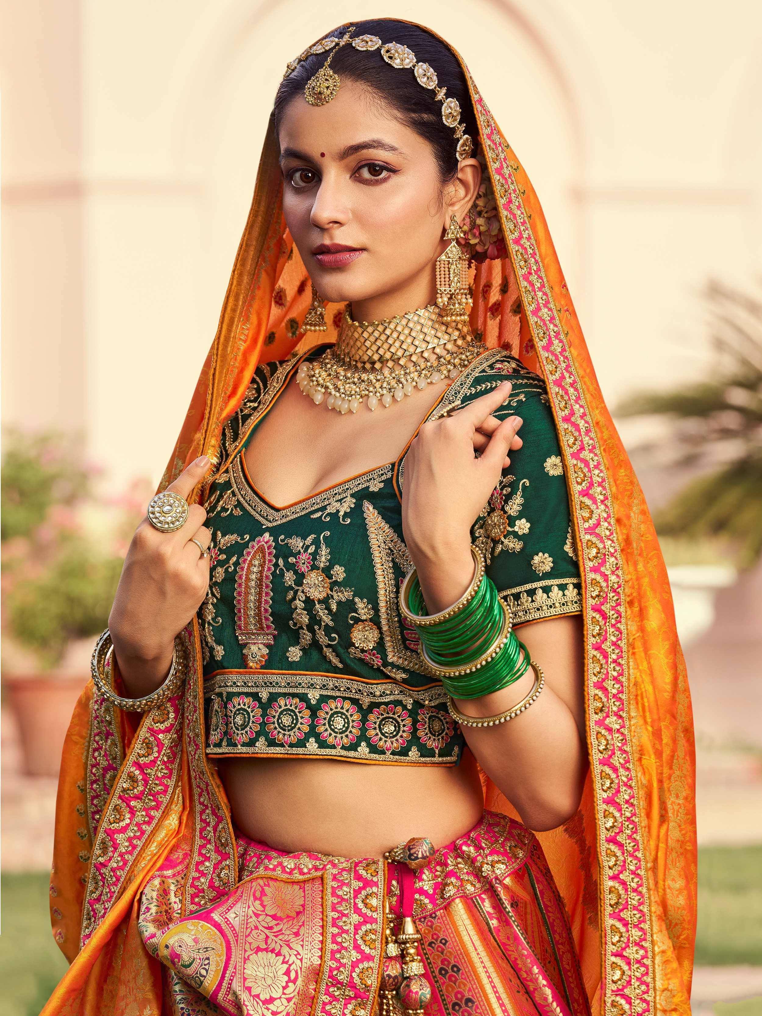 Elegant Indian bride in green and pink embroidered lehenga choli with gold jewelry and orange dupatta