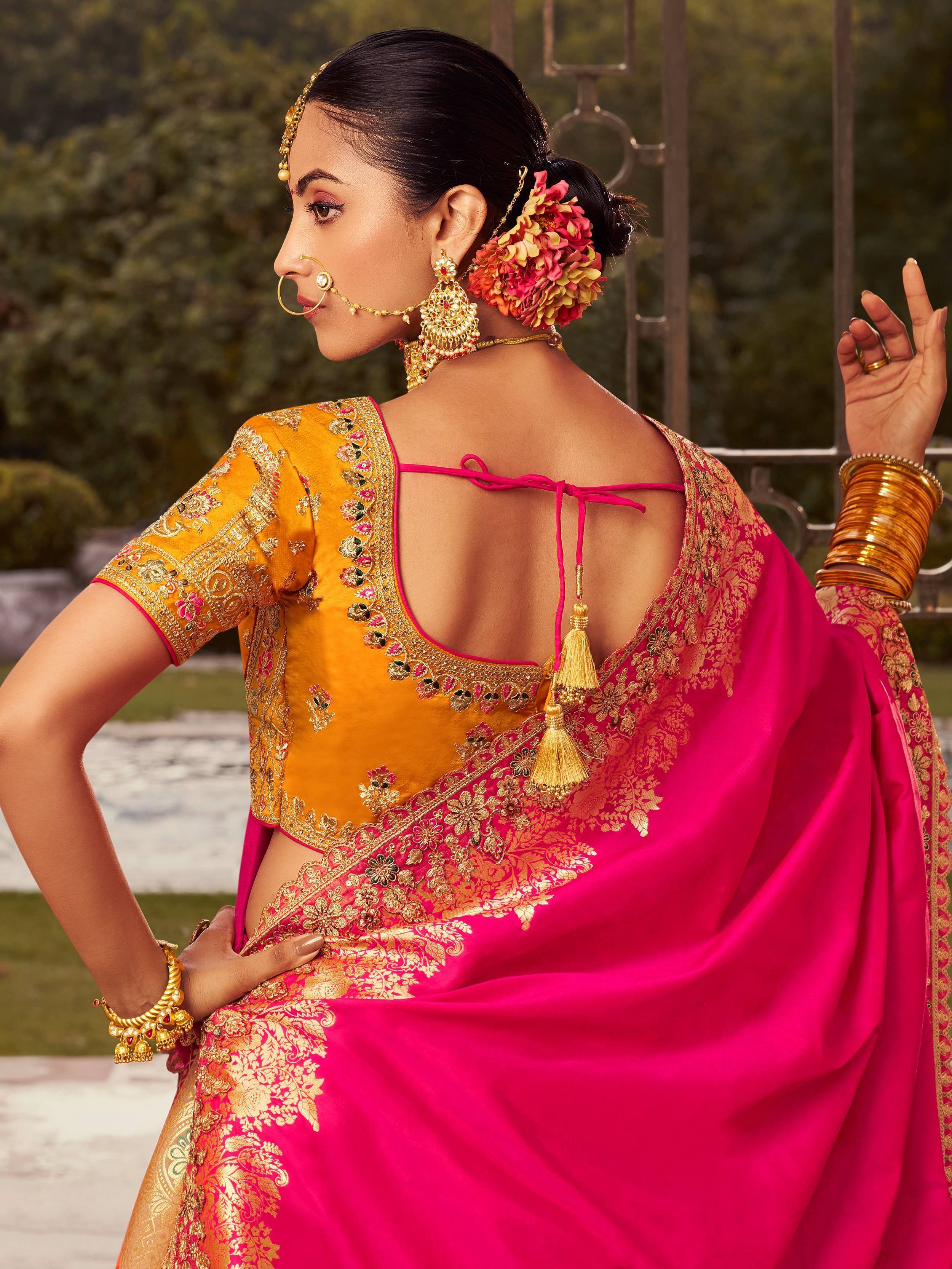 Woman in vibrant pink and gold embroidered saree with floral hair accessory and traditional jewelry
