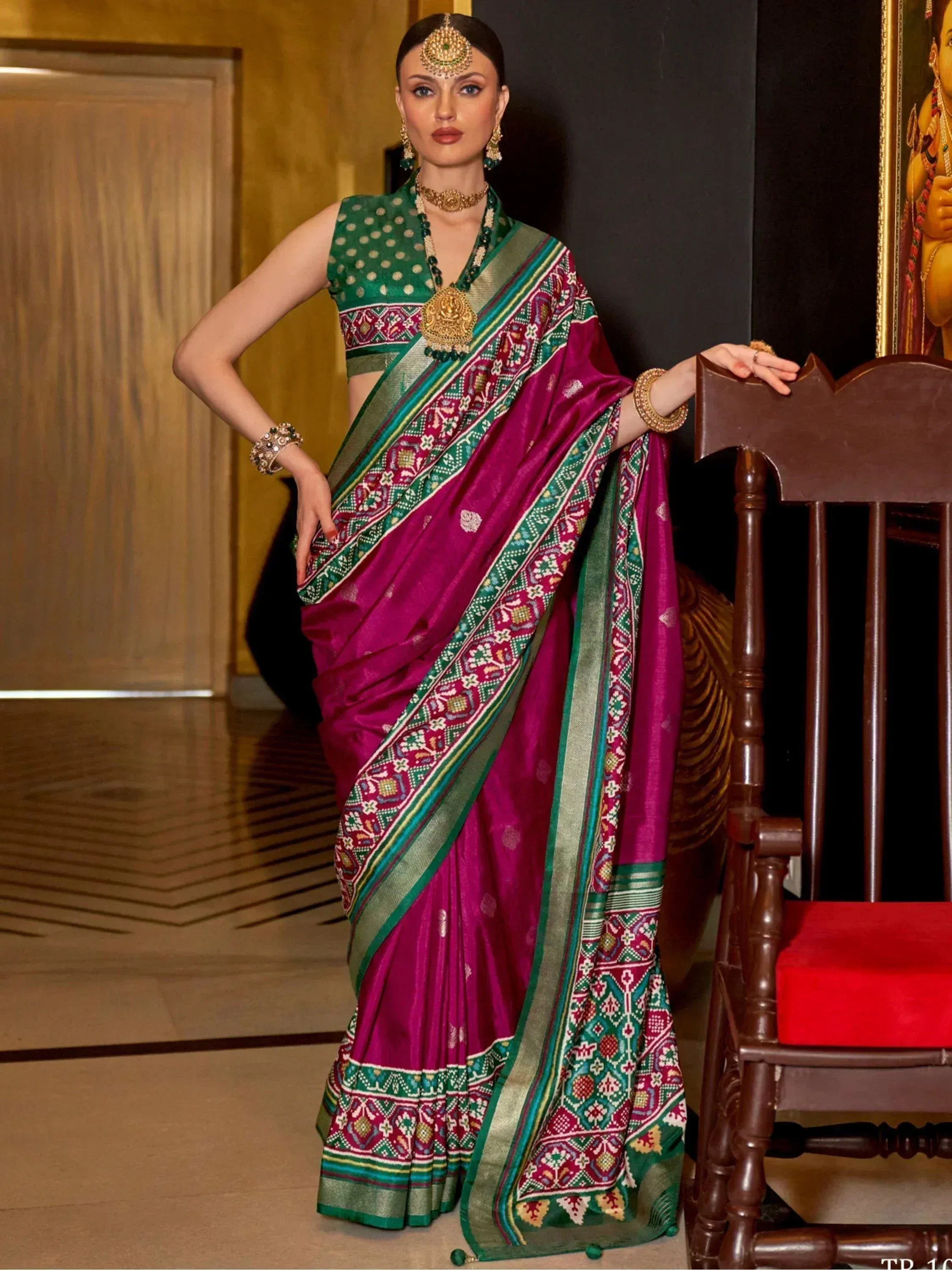Woman in vibrant magenta and green ethnic saree with intricate embroidery, styled with traditional jewelry for festive occasions.