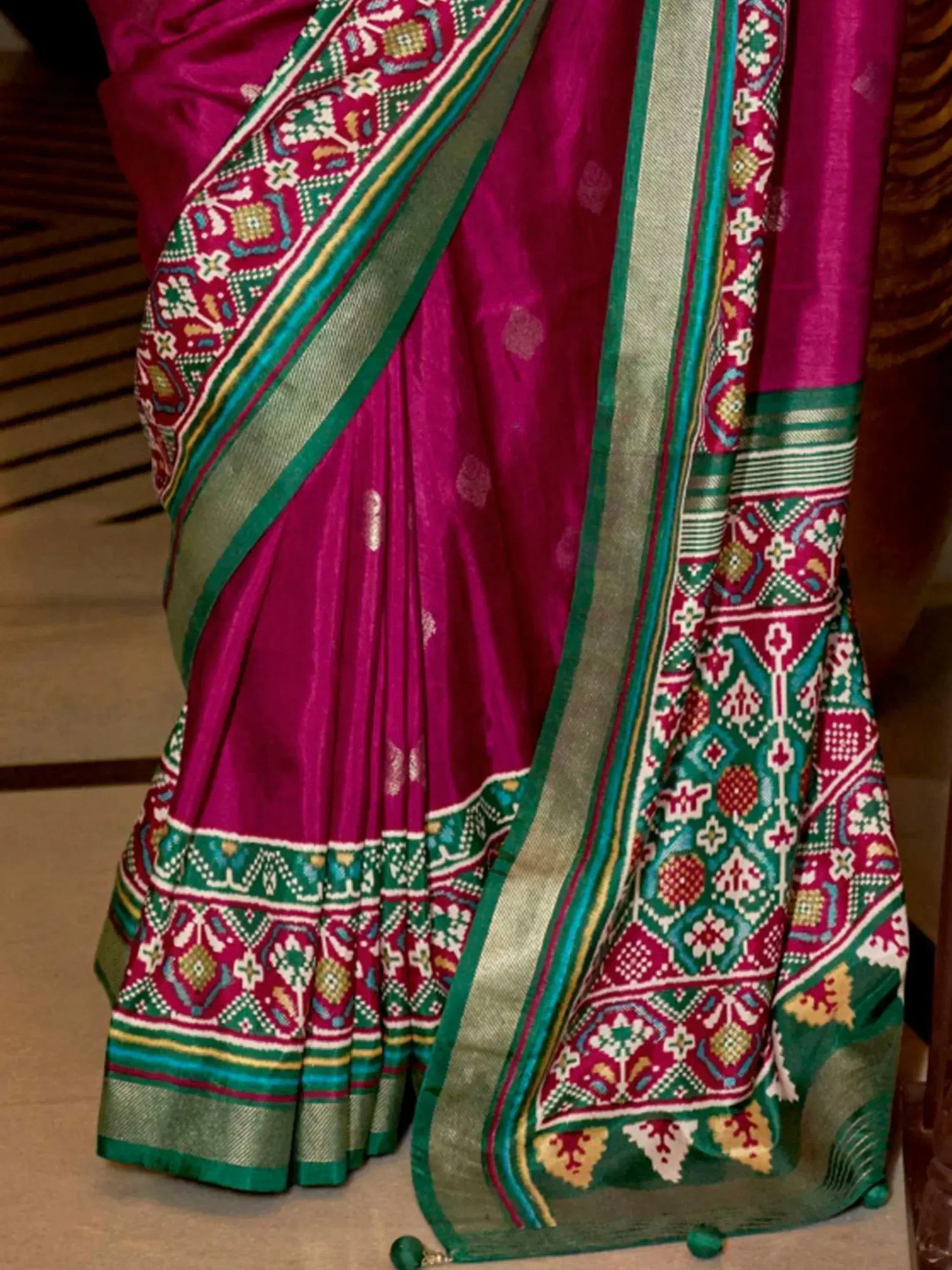 Vibrant magenta saree with intricate green, gold, and white geometric border, perfect for Indian ethnic wear.