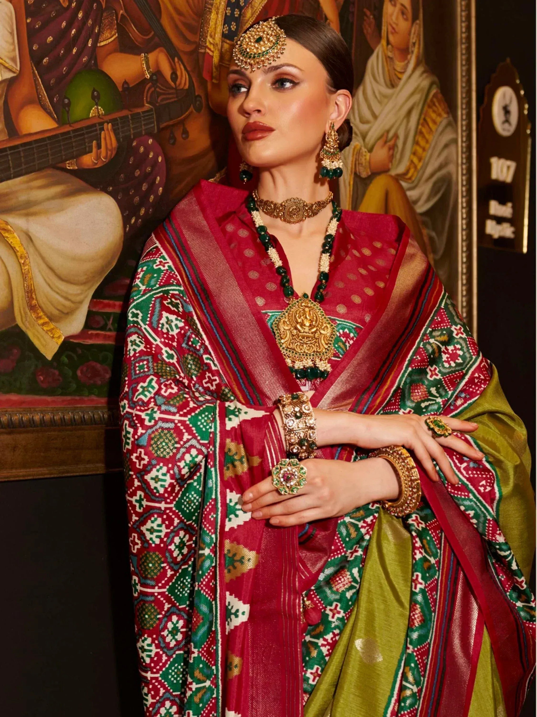 Woman in vibrant red and green ethnic saree with gold jewelry, traditional Indian attire