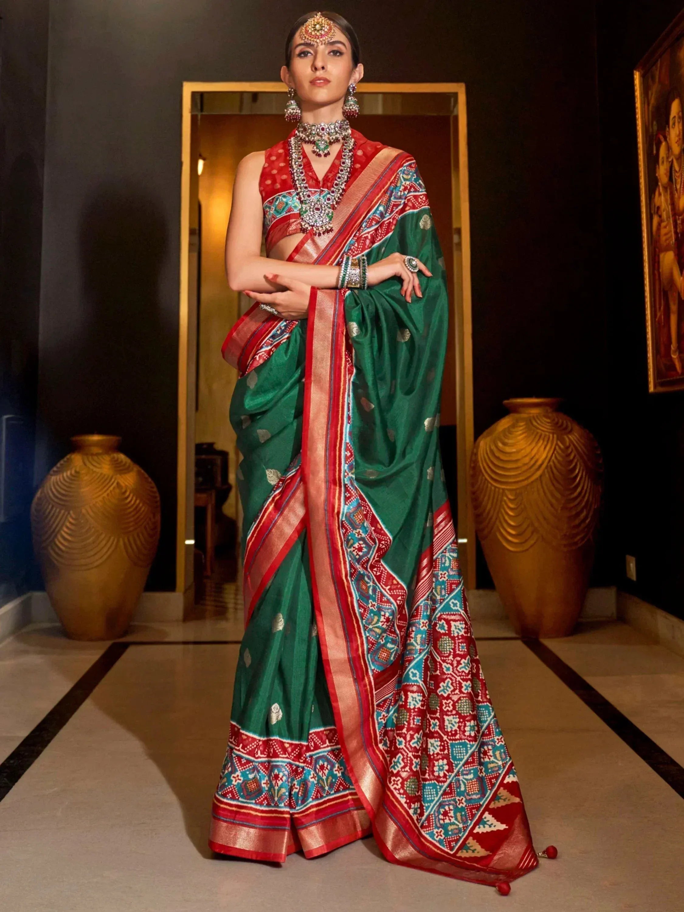 Green and red ethnic saree with intricate patterns, paired with traditional jewelry for festive occasions