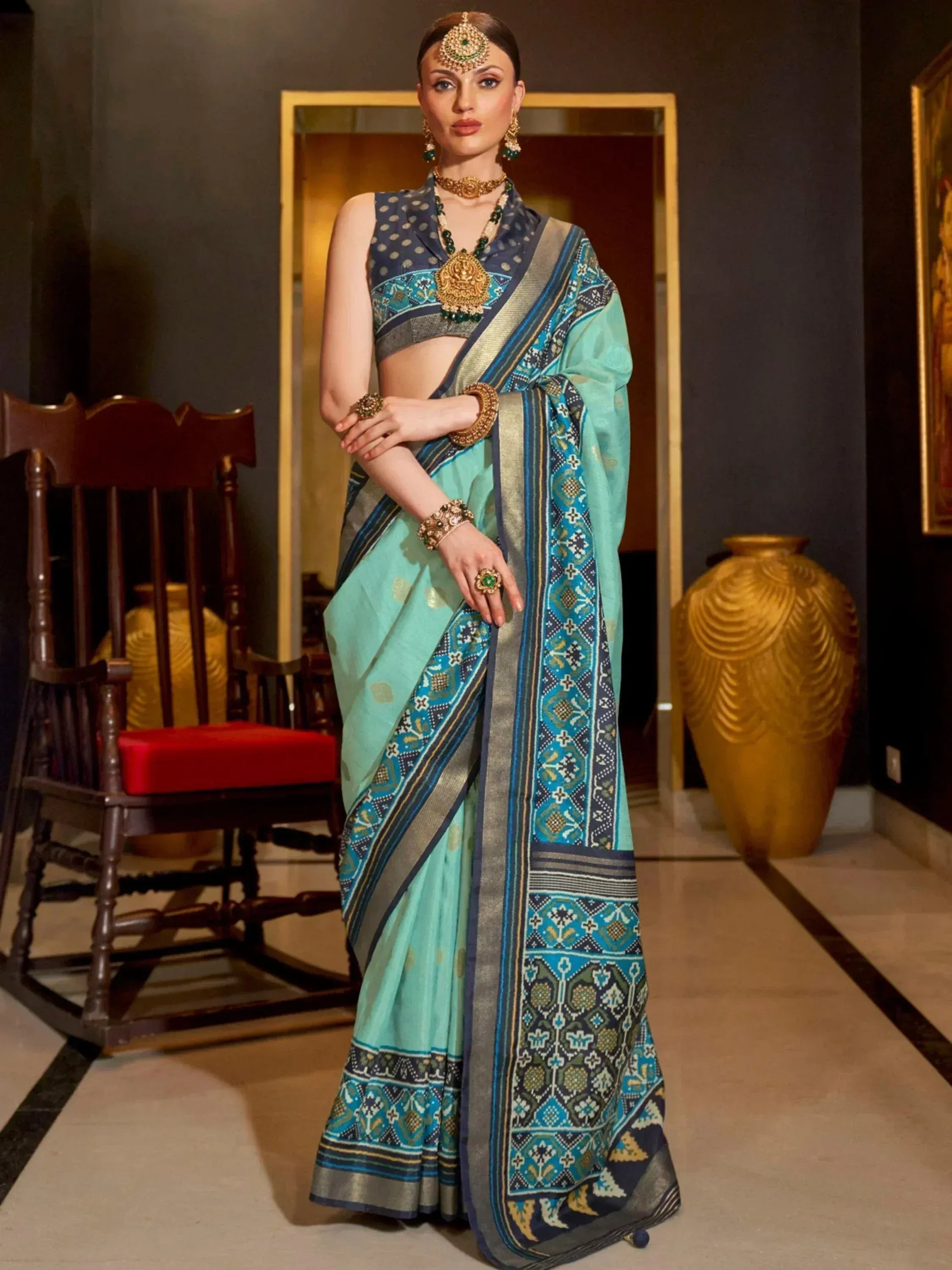 Woman in mint green saree with blue geometric border, paired with sleeveless blouse and traditional jewelry