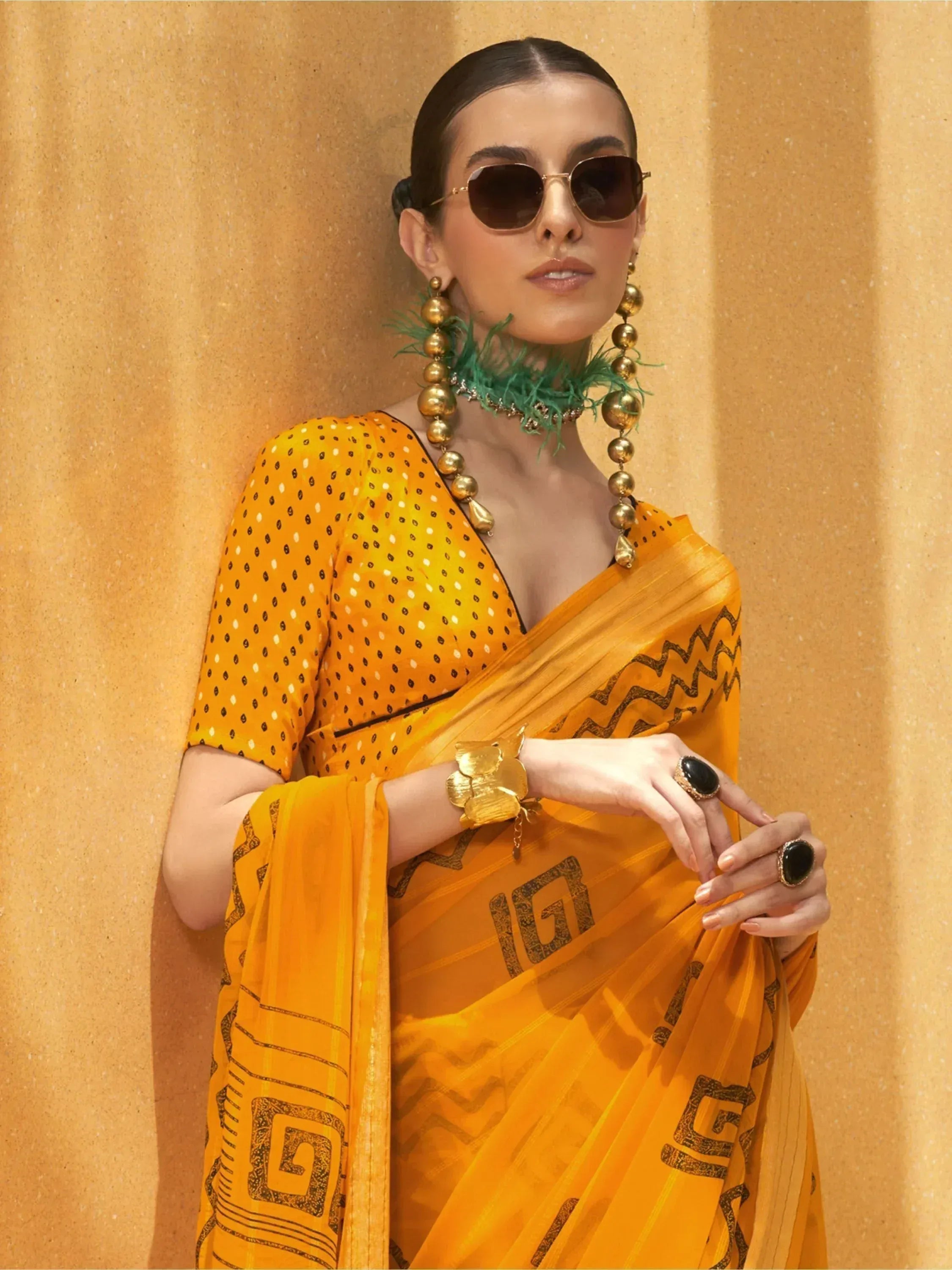 Stylish yellow saree with black geometric print, paired with statement gold jewelry and sunglasses