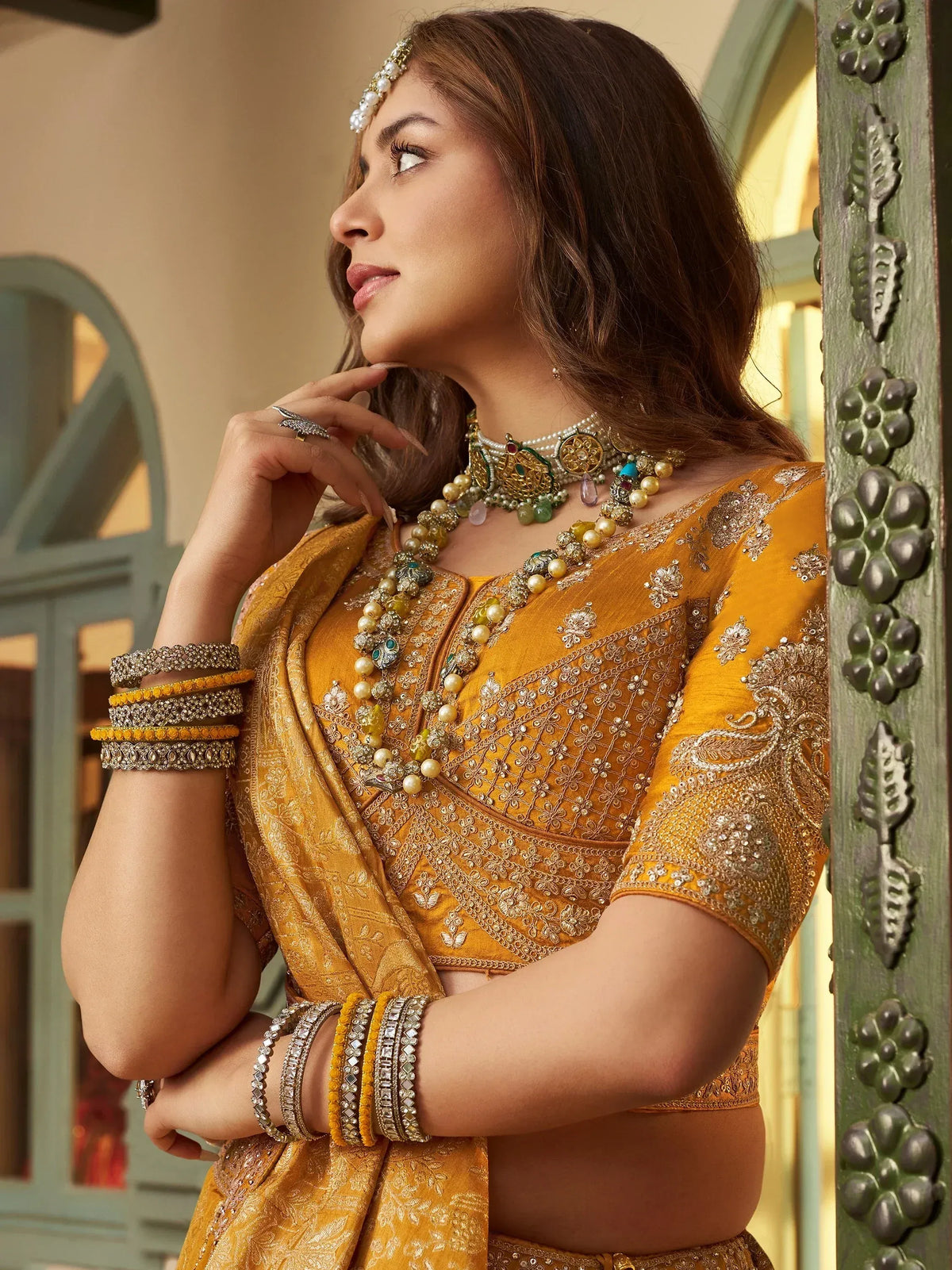 Woman in mustard yellow embroidered lehenga choli with pearl and gemstone jewelry, traditional Indian ethnic wear