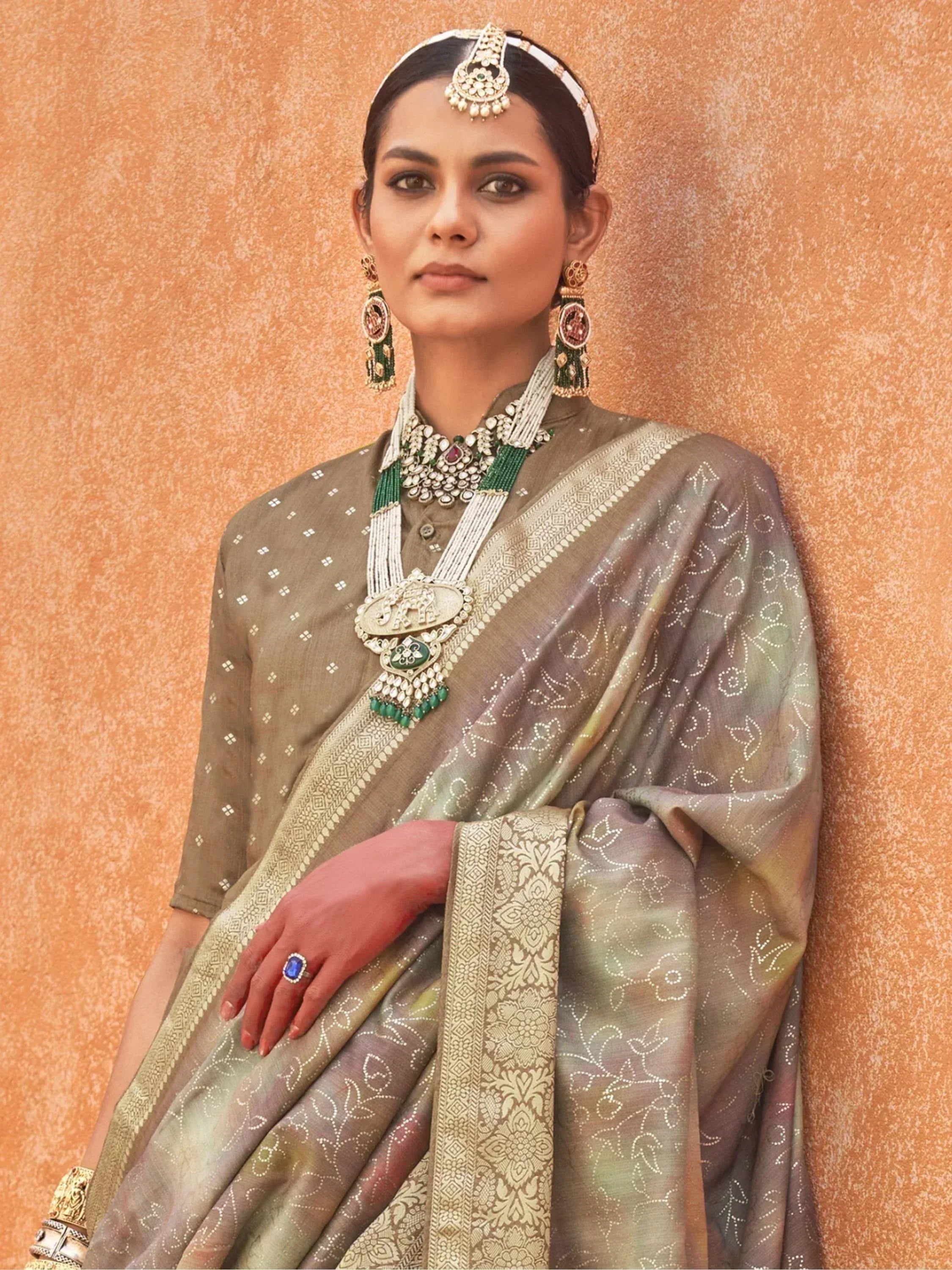 Woman in olive green embroidered saree with gold border, traditional Indian jewelry, and maang tikka
