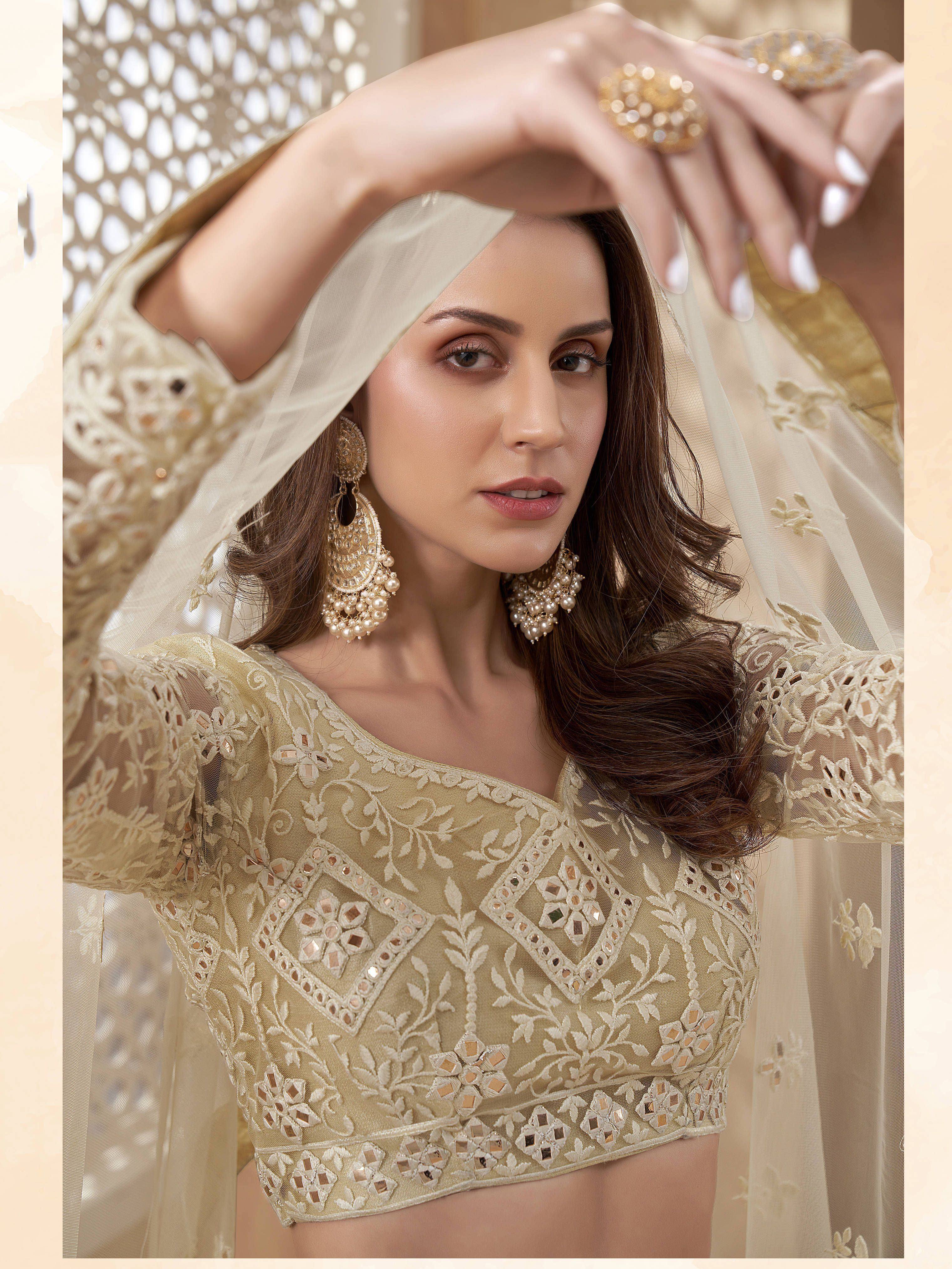 Elegant beige embroidered lehenga choli with mirror work, sheer dupatta, and gold jewelry for Indian ethnic wear