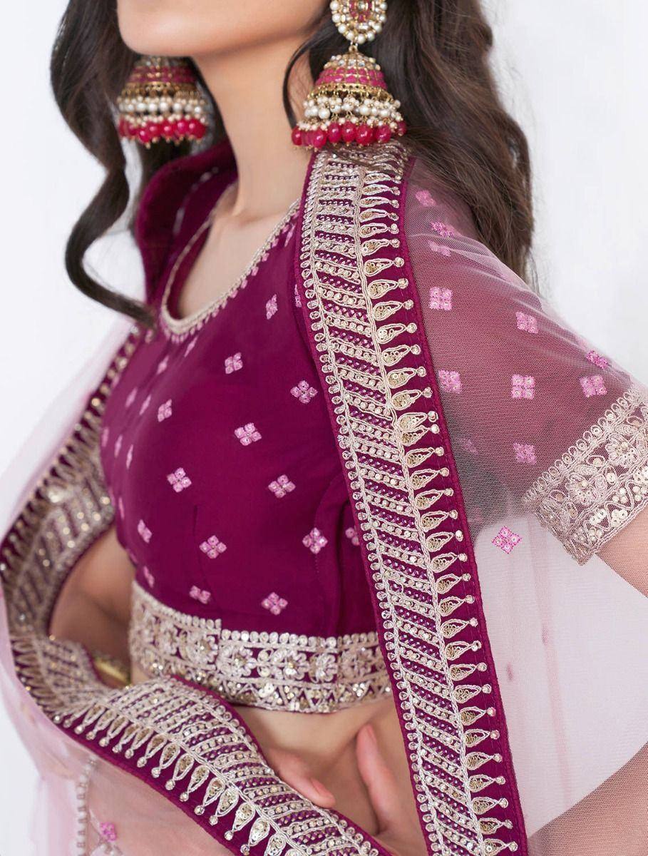 Elegant maroon lehenga choli with gold embroidery and pink net dupatta, paired with traditional jhumka earrings.