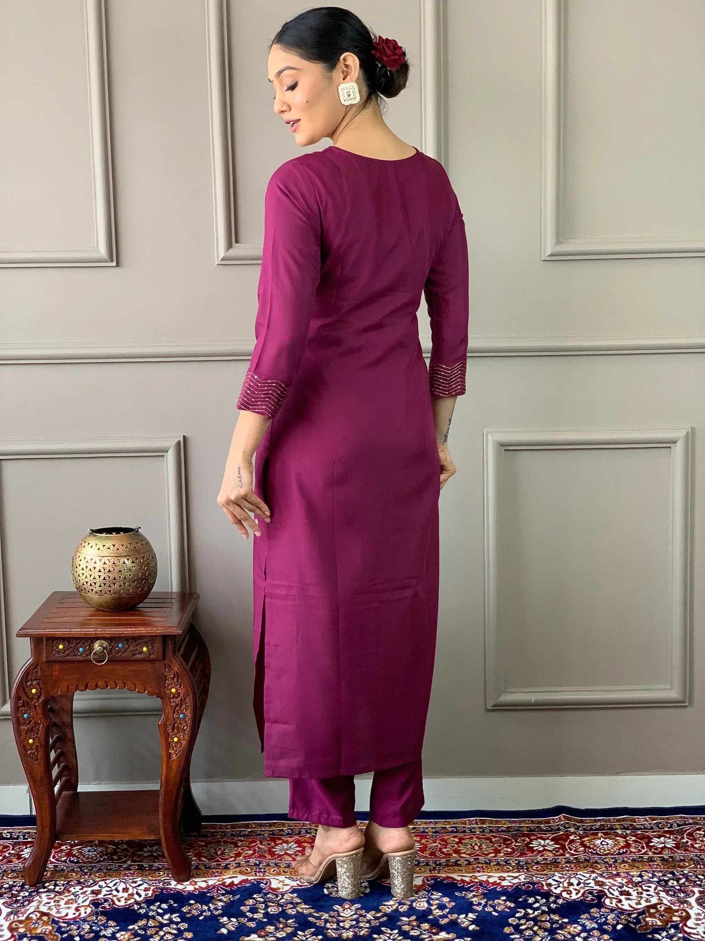 Woman in maroon ethnic kurta with striped cuffs, paired with matching pants, standing on patterned rug
