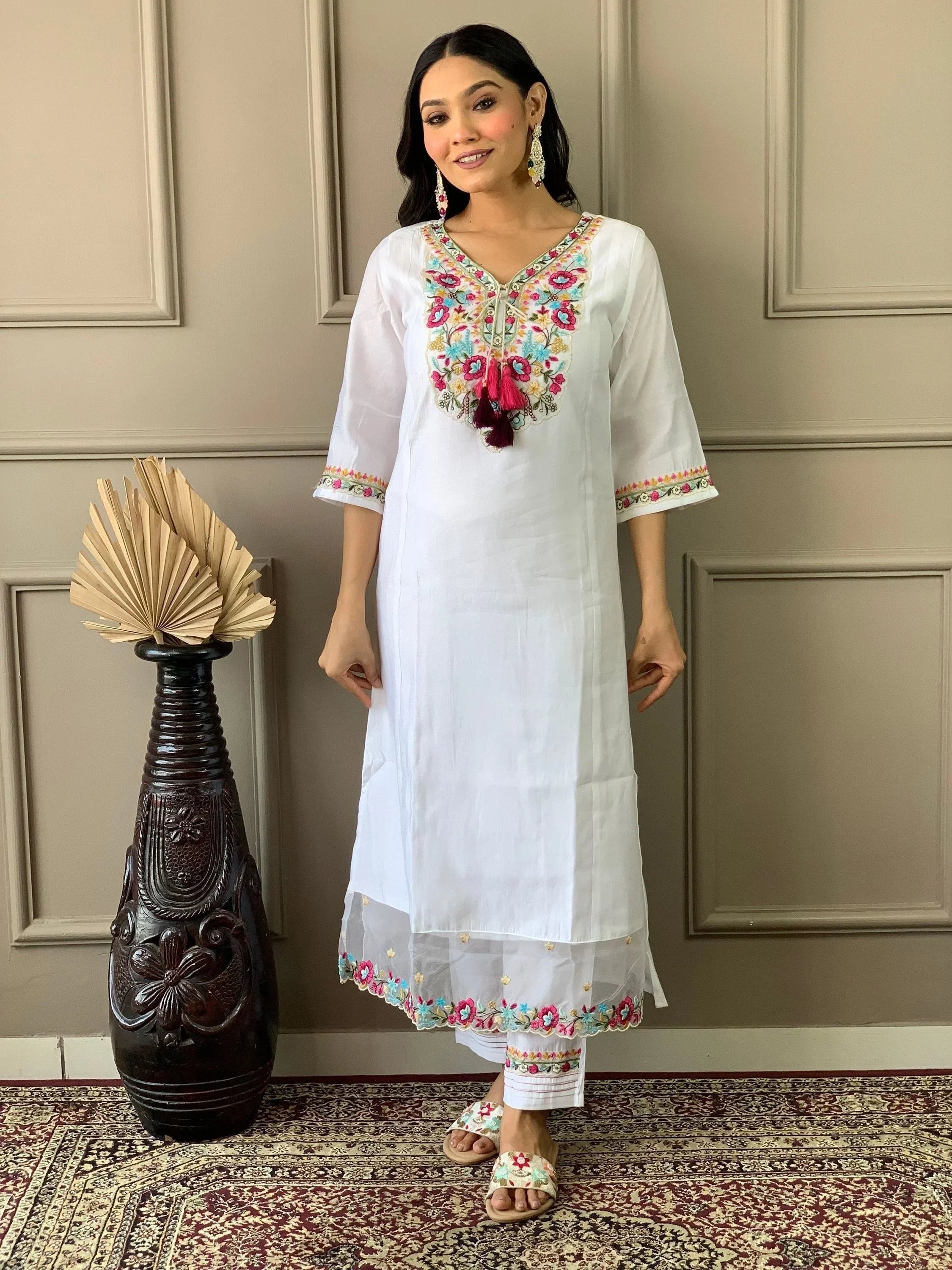 Woman wearing white embroidered kurti and pants, standing indoors on patterned rug