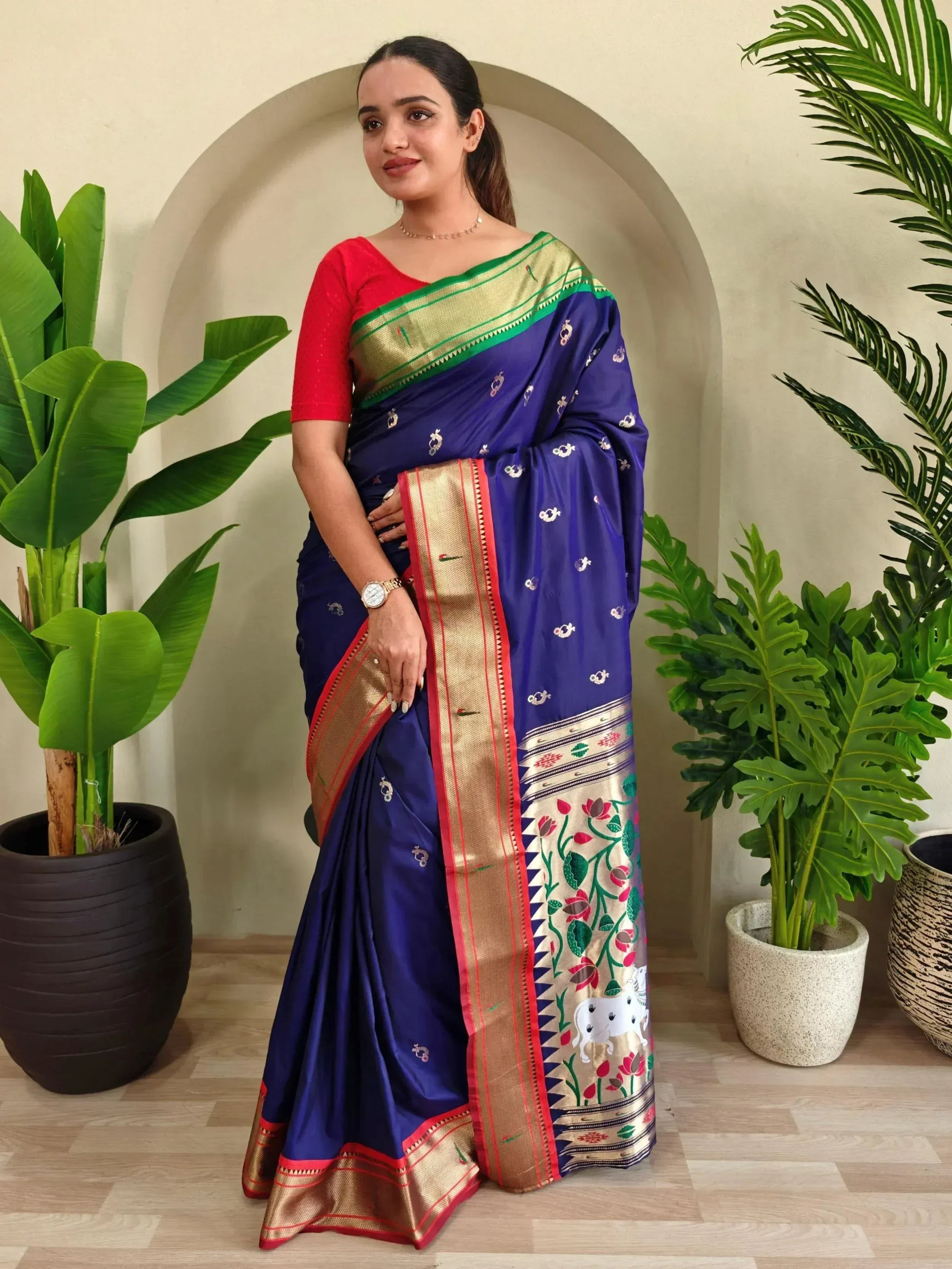 Woman in blue silk saree with gold border, floral motifs, and red blouse, styled for ethnic occasions