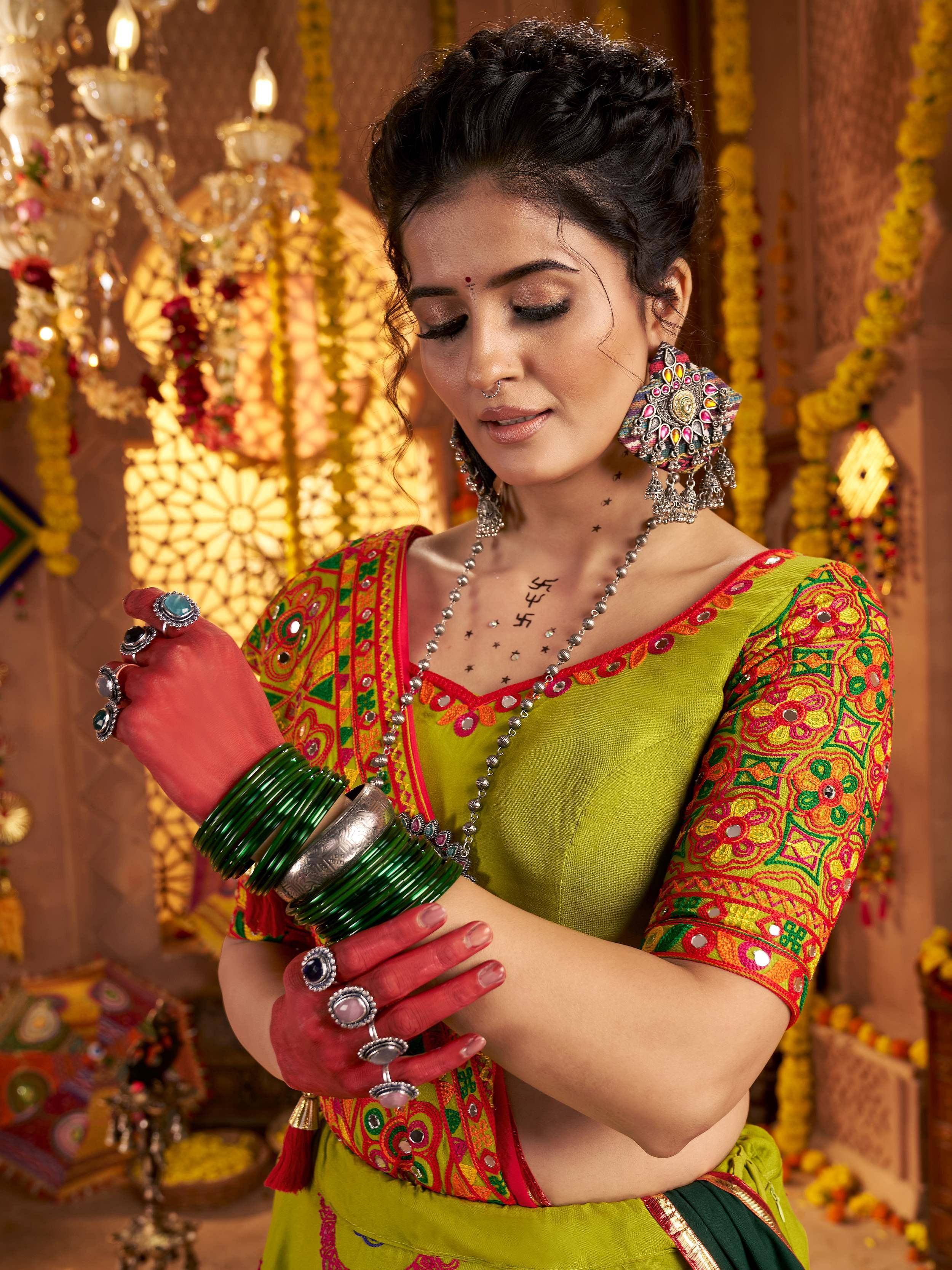 Woman in vibrant green embroidered ethnic wear with mirror work, traditional jewelry, and henna hands