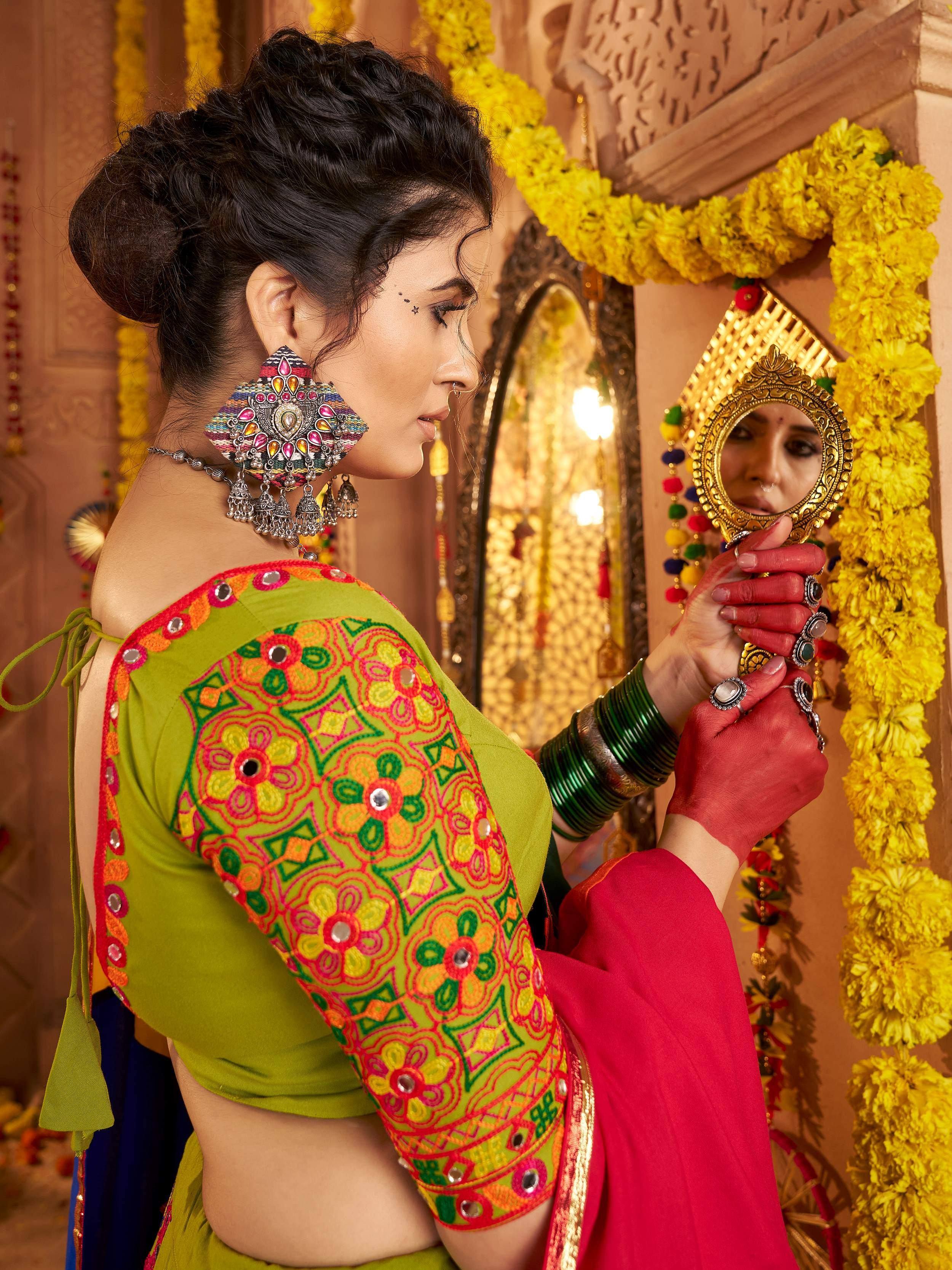 Woman in vibrant green embroidered blouse with mirror work, holding ornate mirror, festive yellow marigold decor