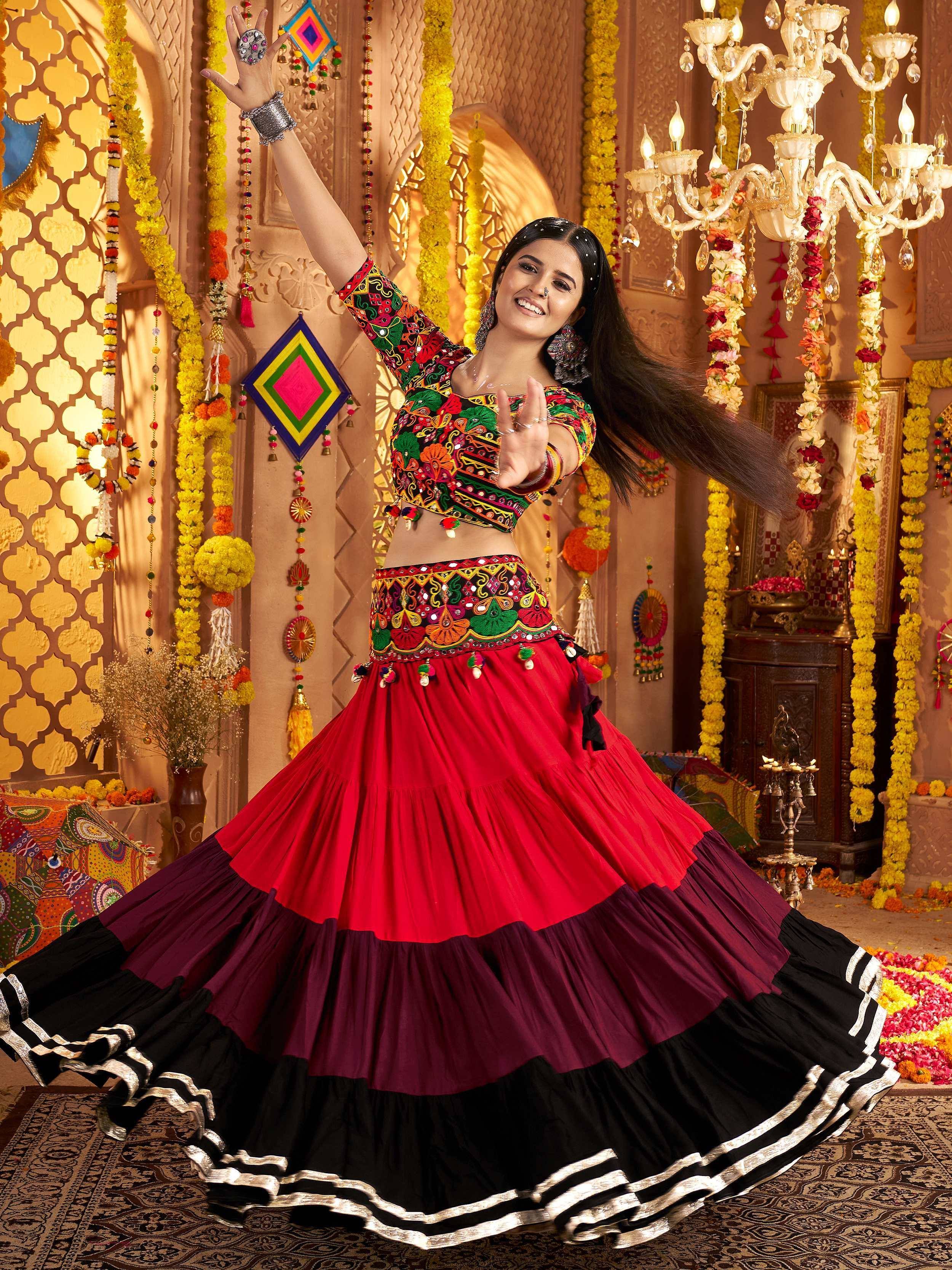 Woman dancing in vibrant red and black embroidered Indian lehenga choli, festive floral decor, traditional ethnic wear