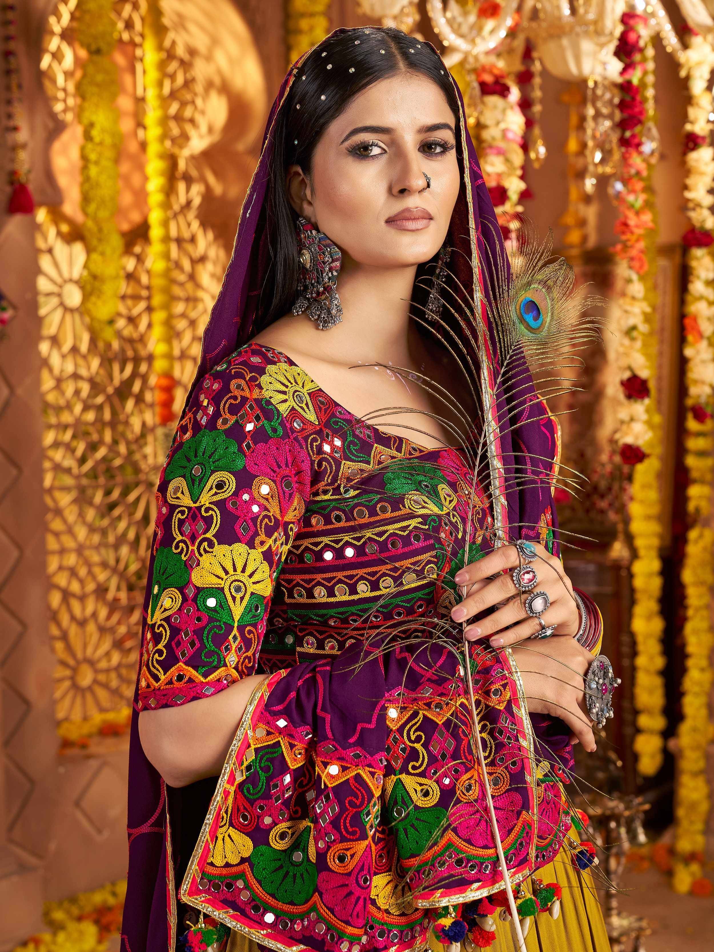 Woman in vibrant purple embroidered ethnic wear with mirror work, holding peacock feather, festive Indian attire