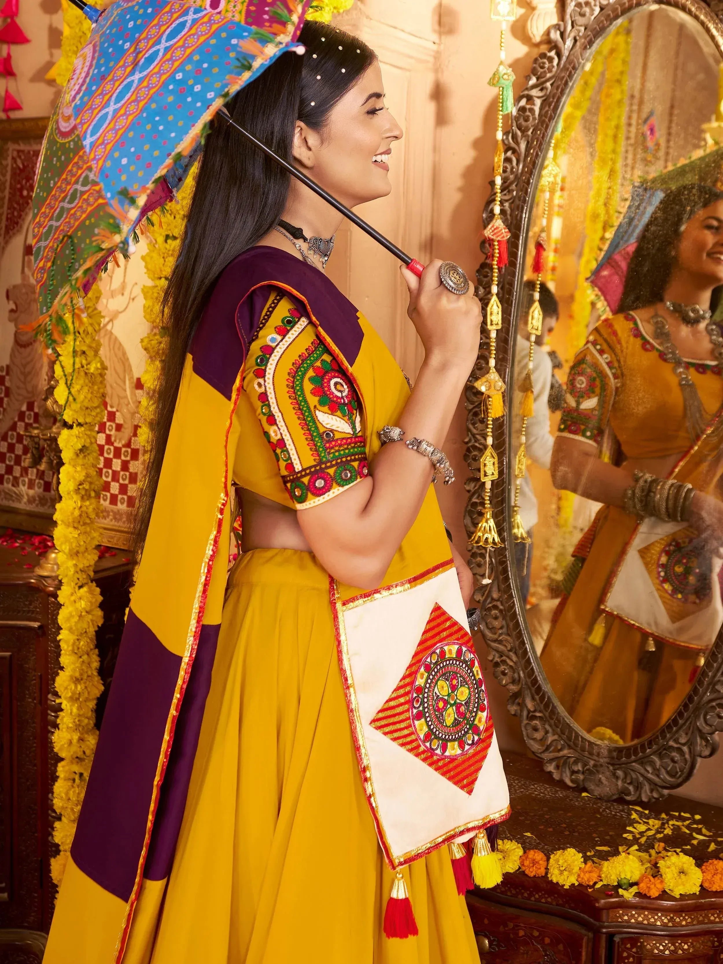 Woman in yellow and purple embroidered lehenga choli holding colorful umbrella, festive Indian ethnic wear