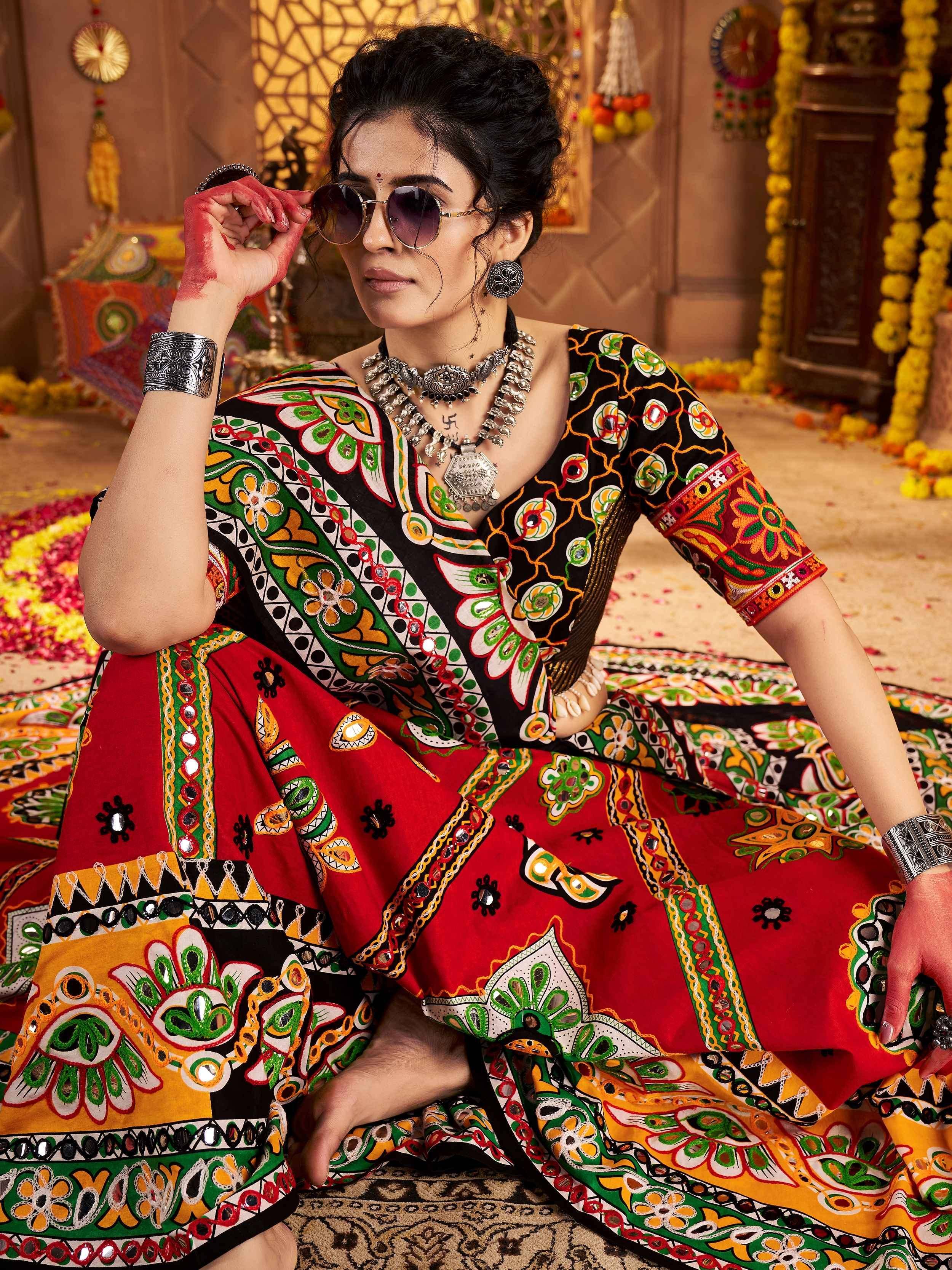 Woman in vibrant ethnic Indian dress with mirror work, floral patterns, and traditional jewelry, styled for festive occasions.