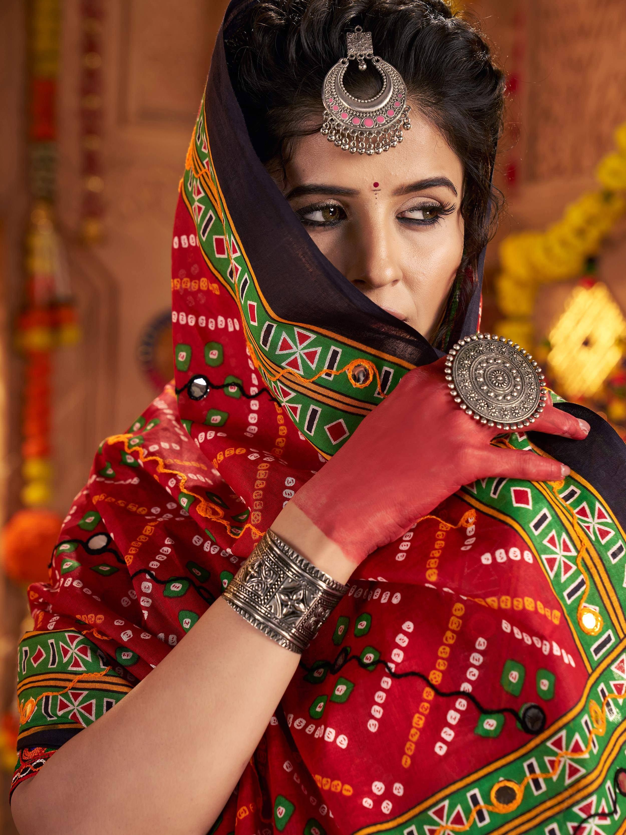 Woman in vibrant red and green ethnic saree with traditional silver jewelry and bindi, showcasing Indian cultural attire.