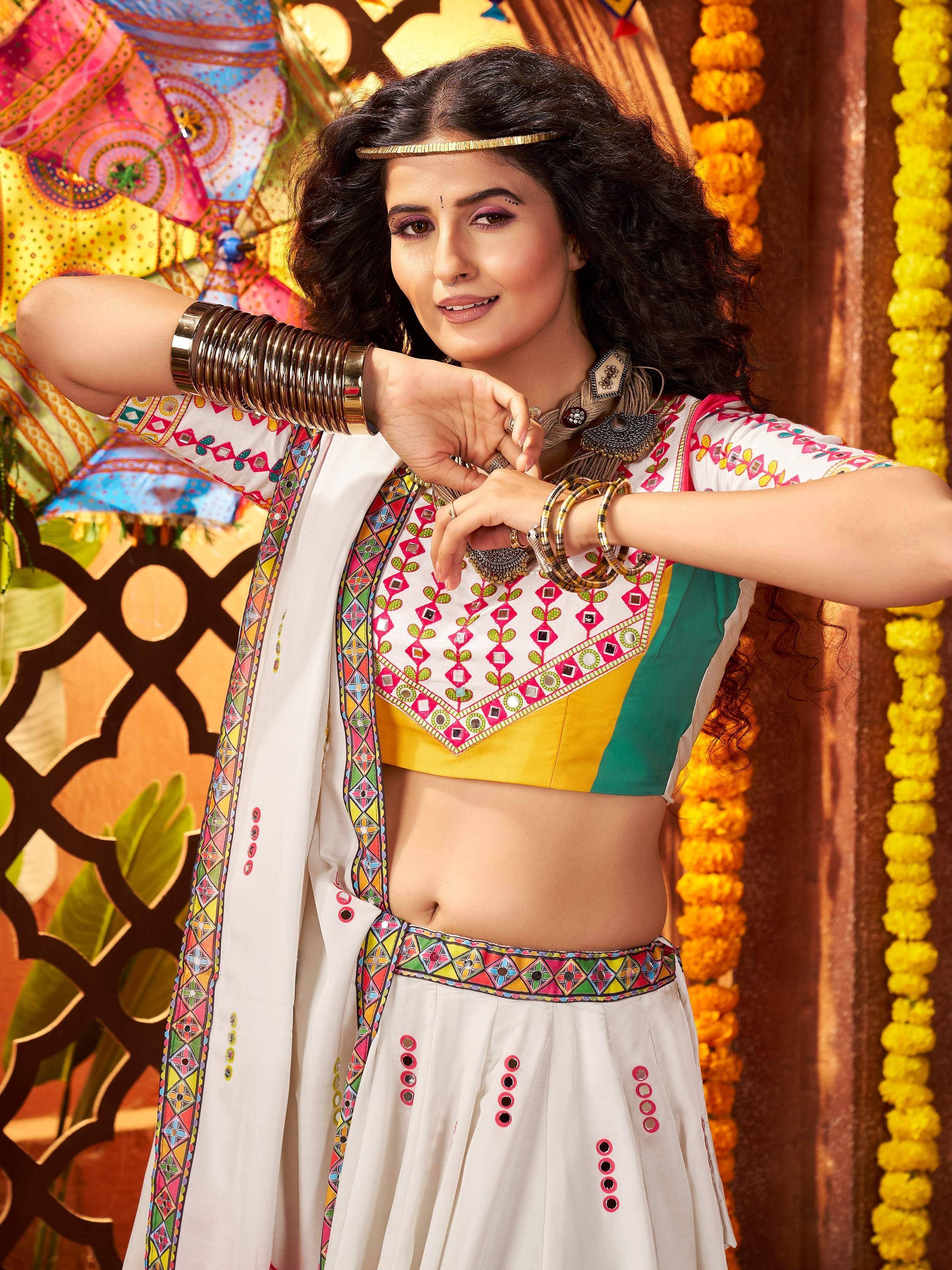 Woman in colorful embroidered Indian ethnic wear with mirror work, bangles, and floral backdrop