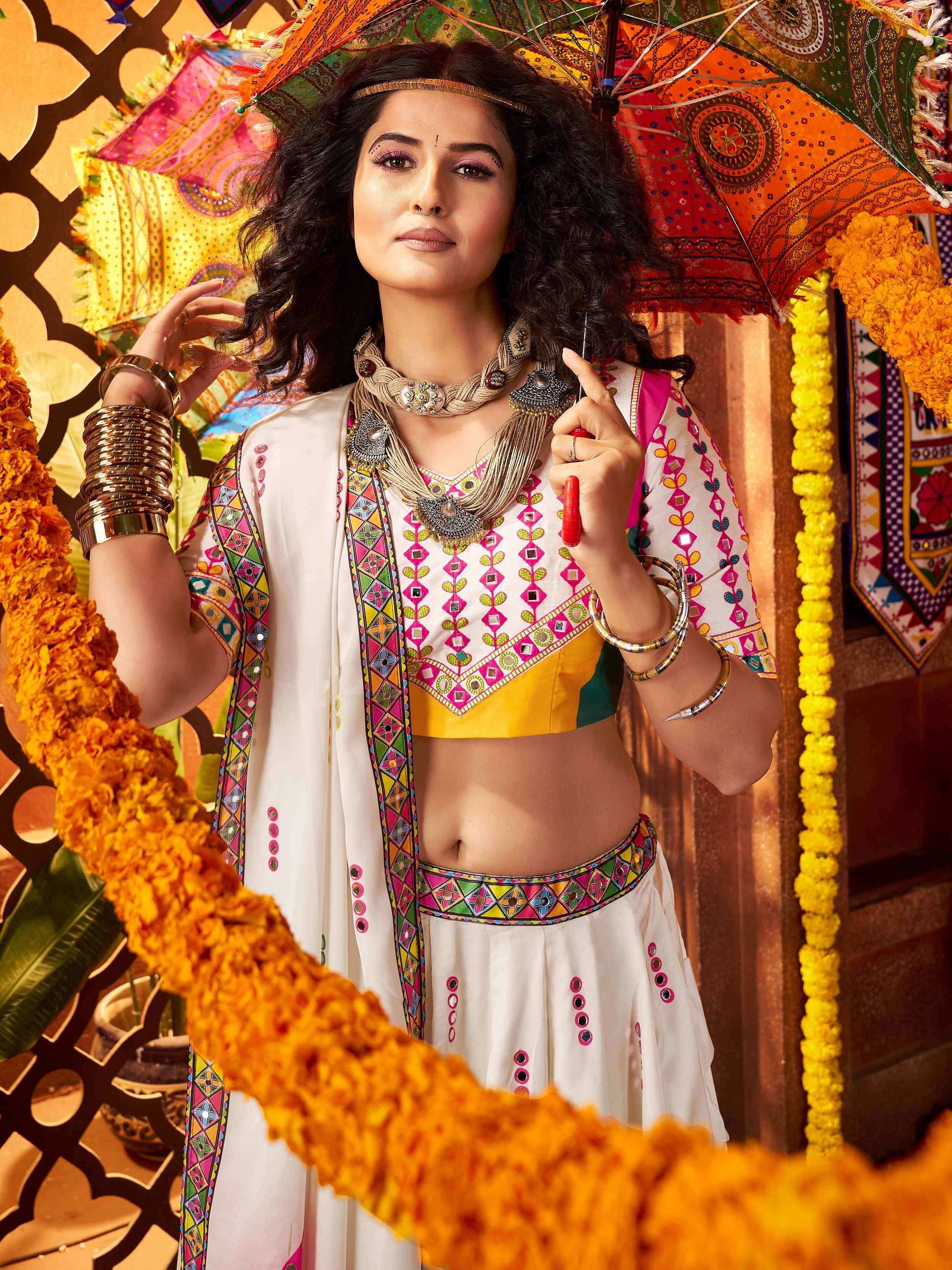 Woman in colorful Indian ethnic wear with mirror work, holding decorative umbrella, festive marigold garlands