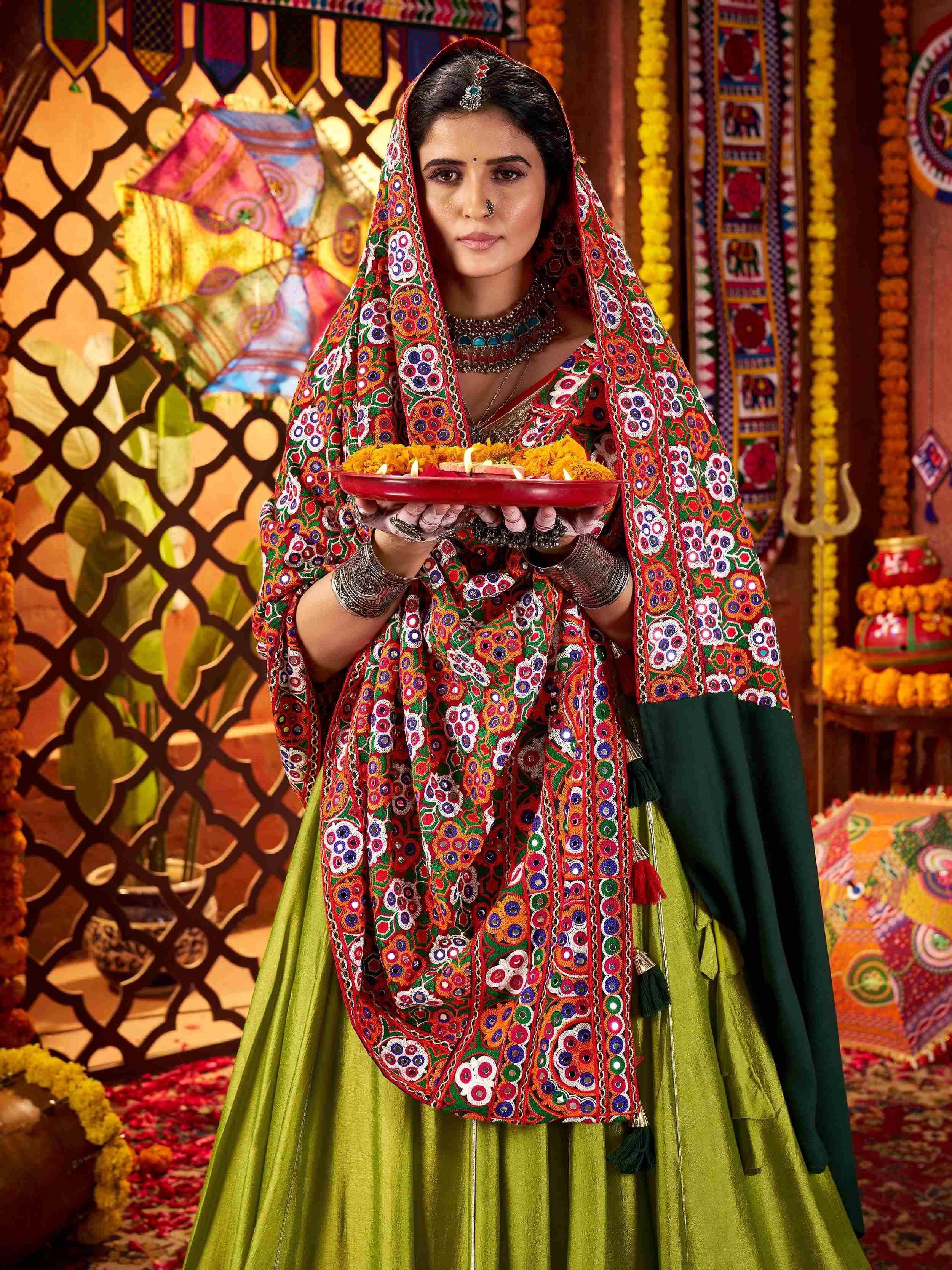 Woman in vibrant Indian ethnic wear with mirror work, holding ceremonial plate, festive backdrop