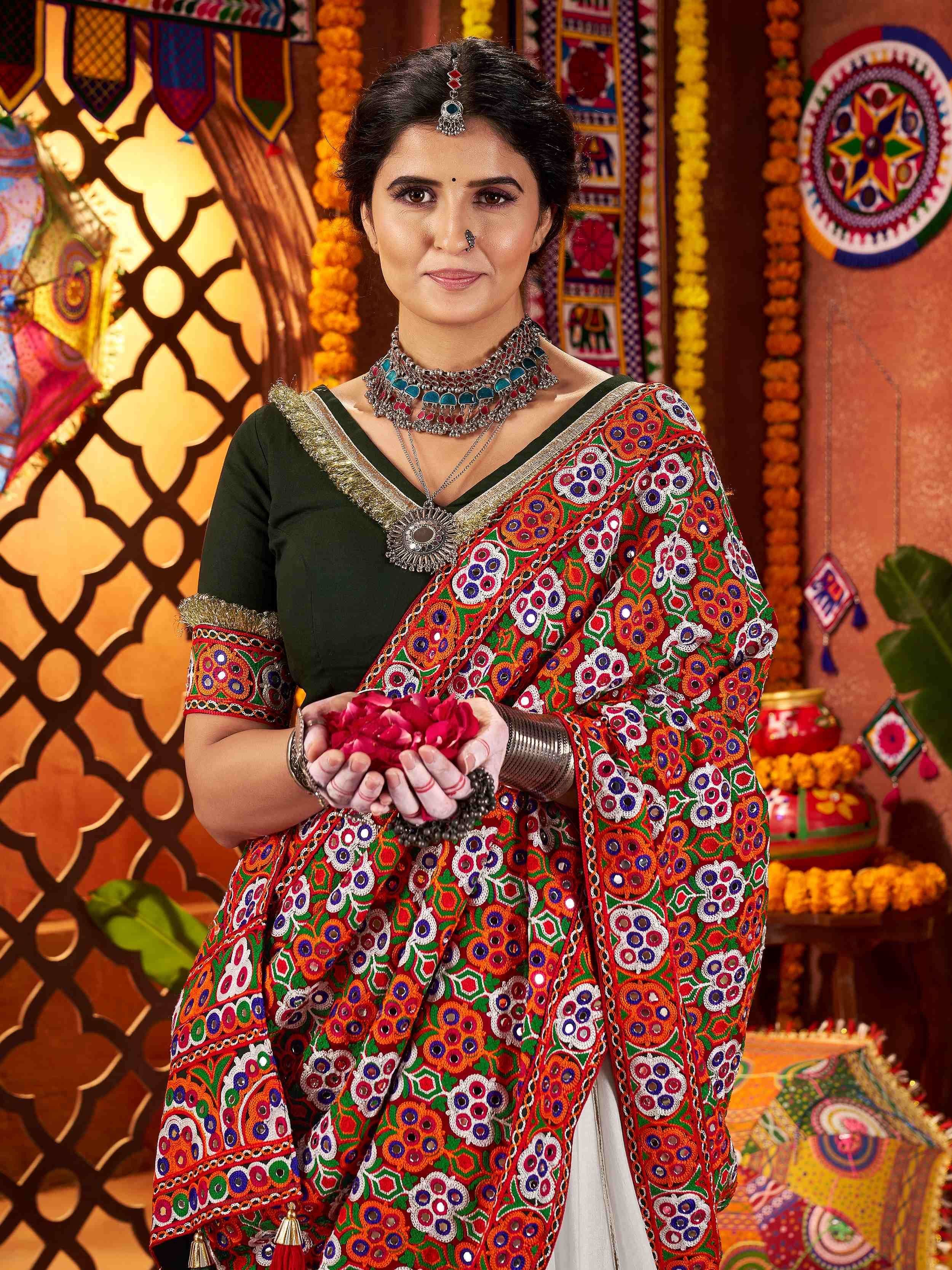 Woman in vibrant mirror-work ethnic saree with traditional jewelry, holding rose petals, festive Indian decor background