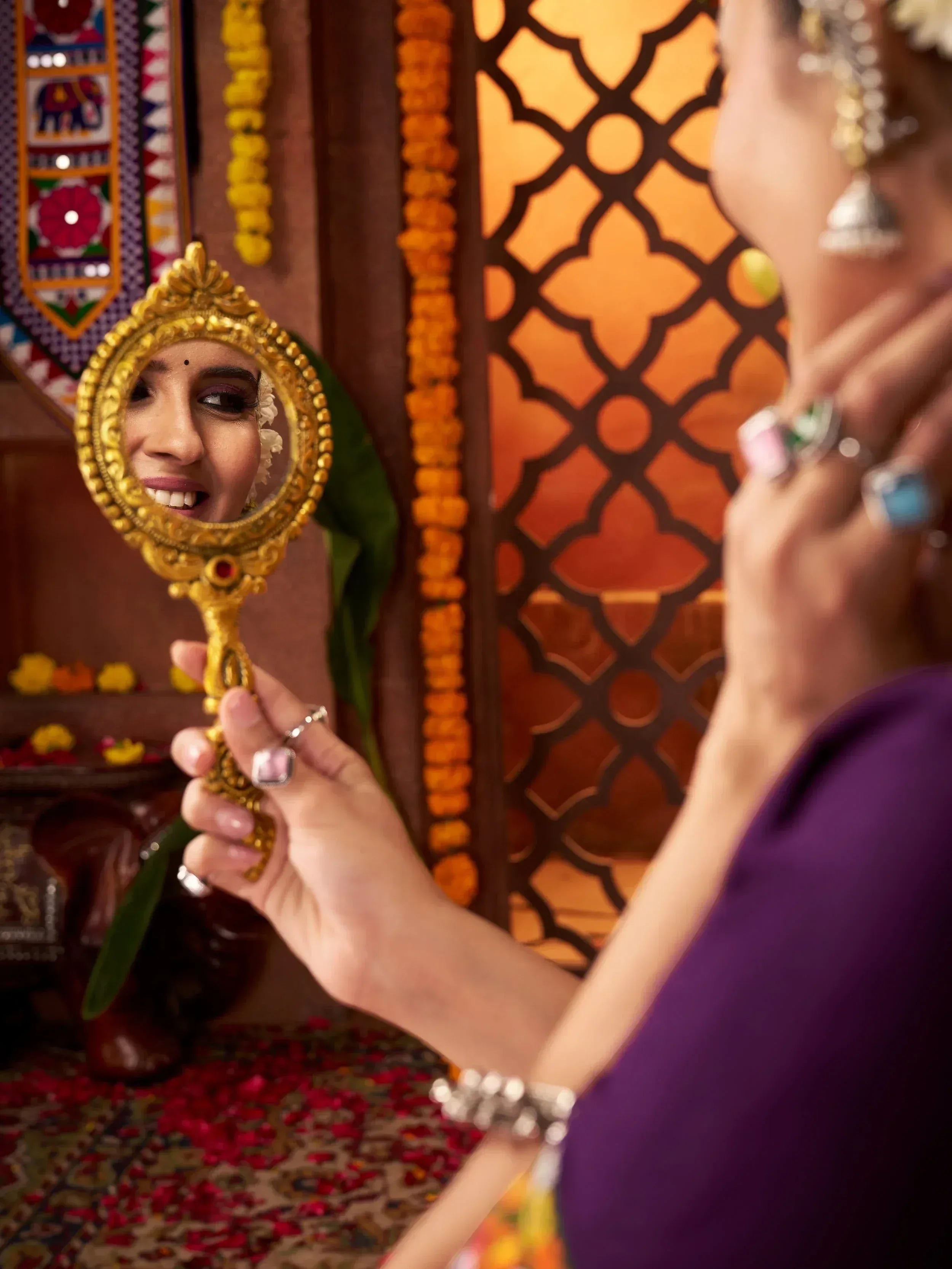 Woman in purple ethnic gown admiring herself in ornate gold mirror with floral decor