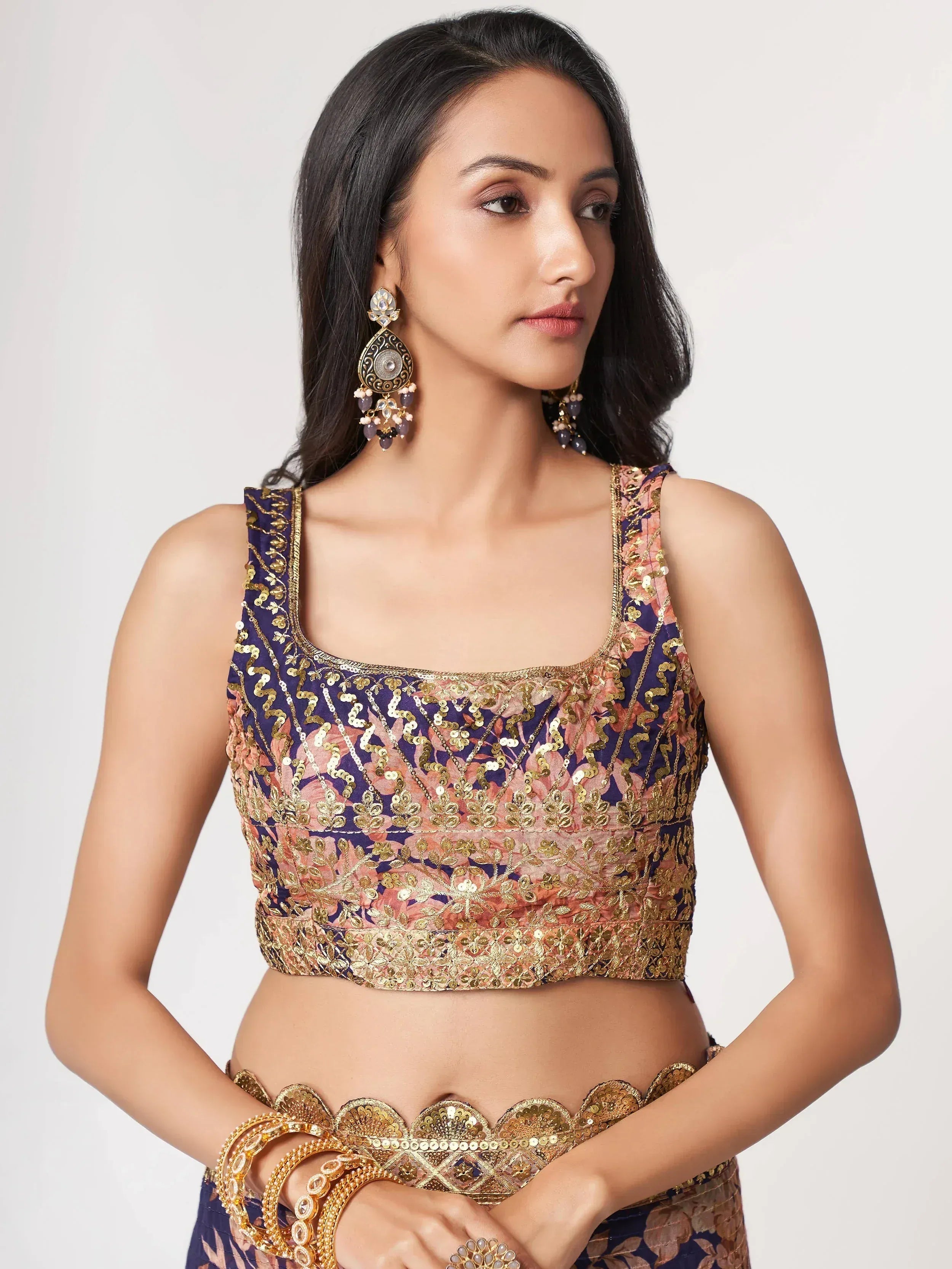 Woman in embroidered purple and pink lehenga choli with gold sequins and matching earrings