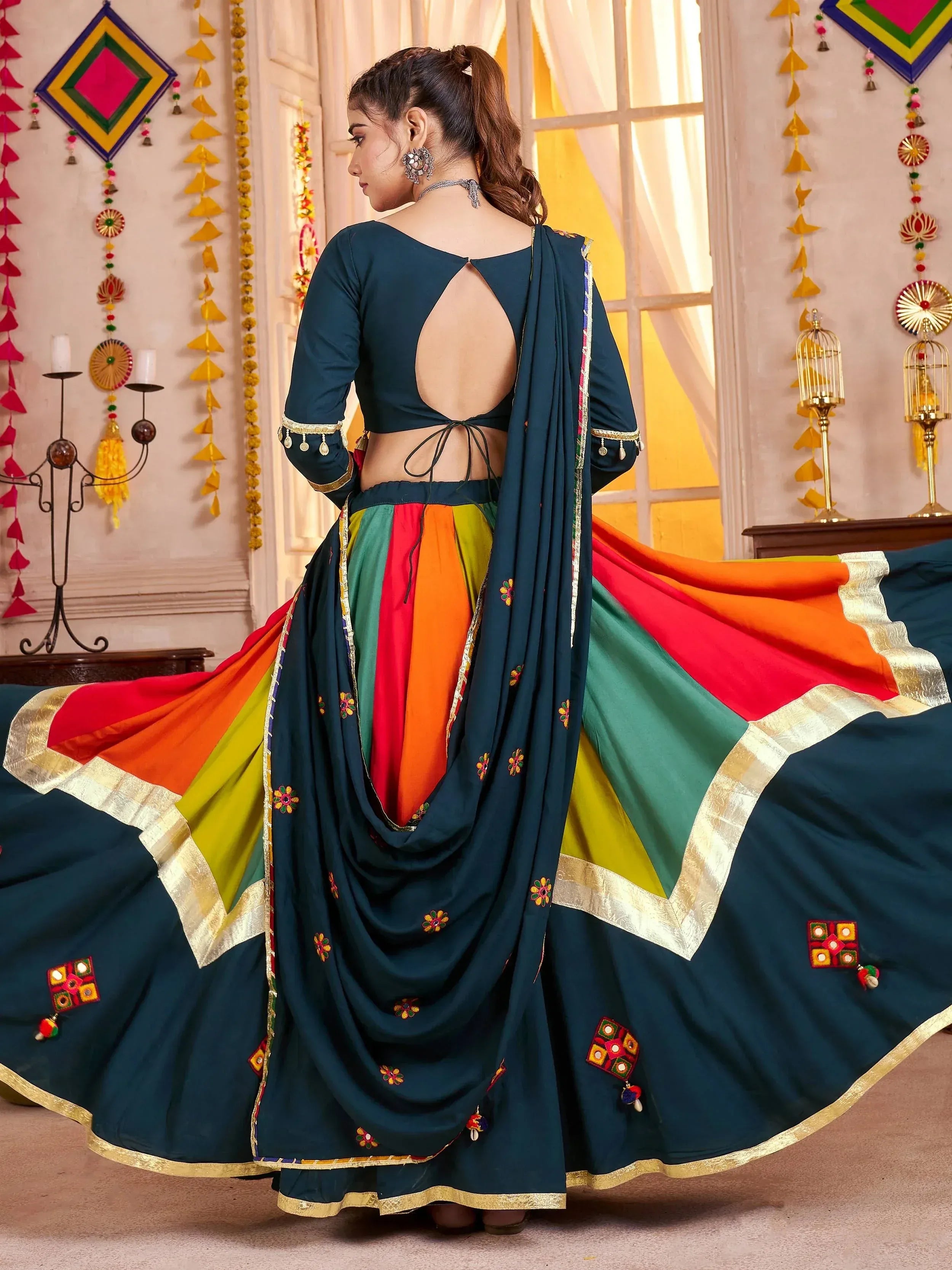 Woman in teal designer lehenga choli with colorful panel skirt and embroidered dupatta, back view