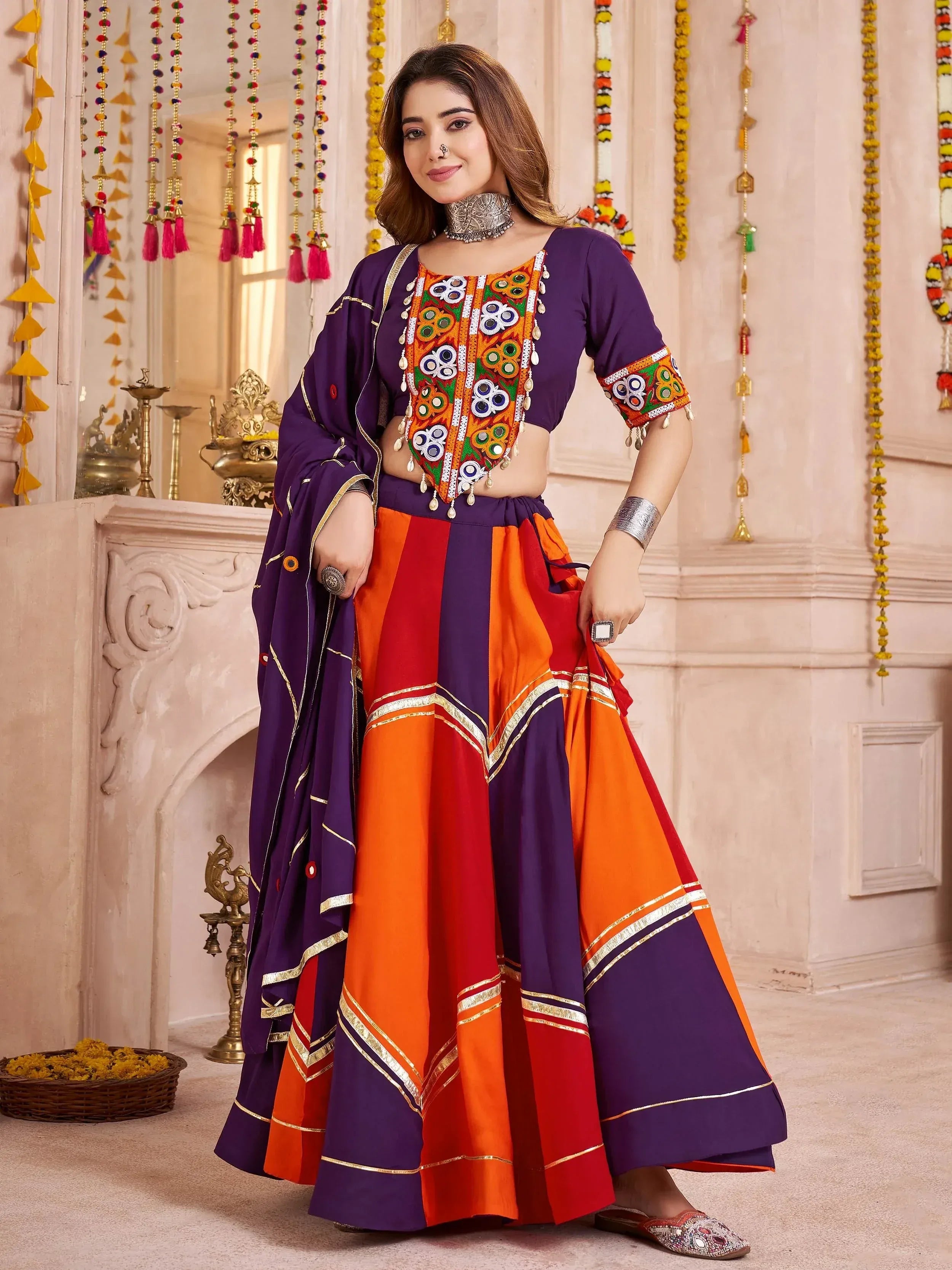 Vibrant purple, orange, and red ethnic sharara set with mirror work and gold trim, perfect for festive occasions.