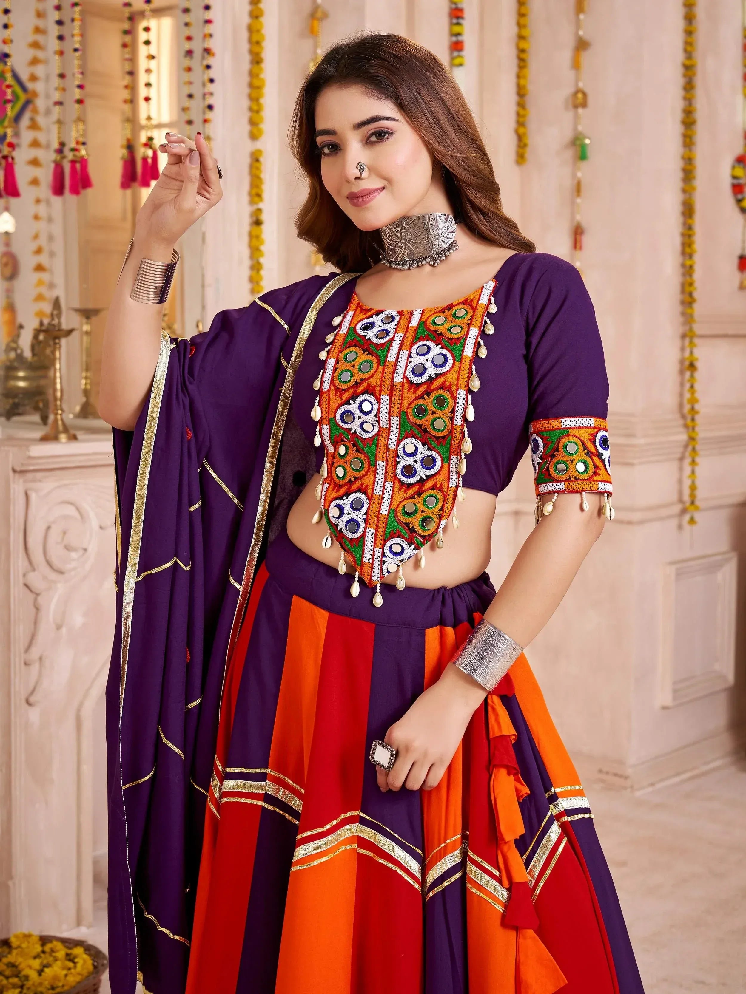 Purple and orange ethnic lehenga choli with mirror work and gold trim, perfect for festive occasions.