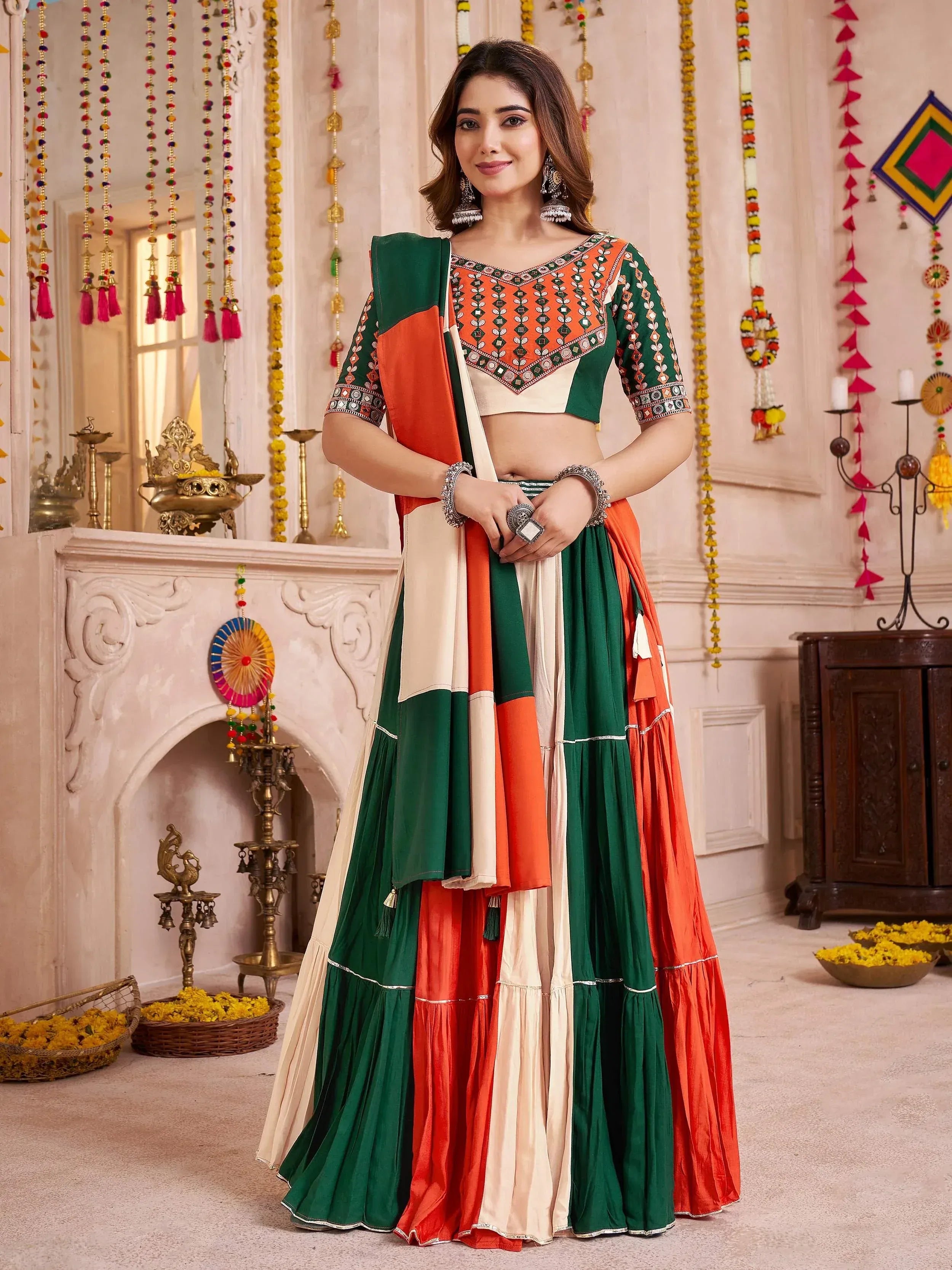 Woman in vibrant green, orange, and cream ethnic lehenga choli with mirror work, perfect for festive occasions.