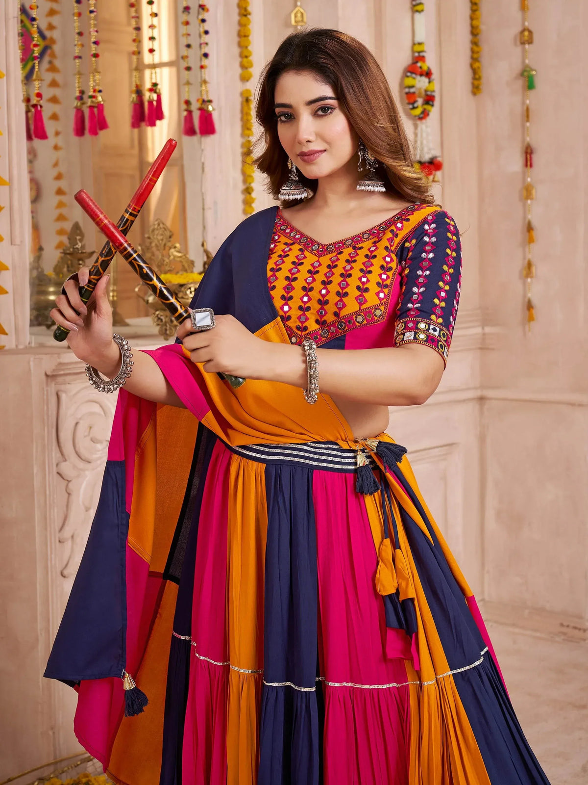 Woman in vibrant Indian ethnic wear with mirror work, holding dandiya sticks for festive celebration