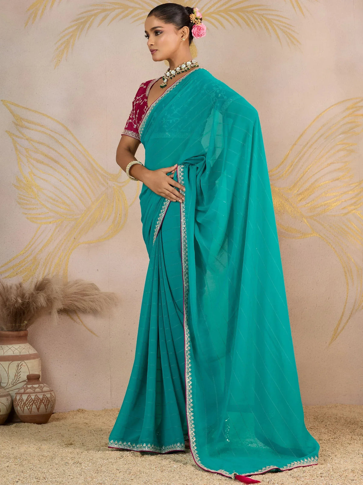 Teal saree with embroidered border and maroon blouse, styled with floral hair accessory