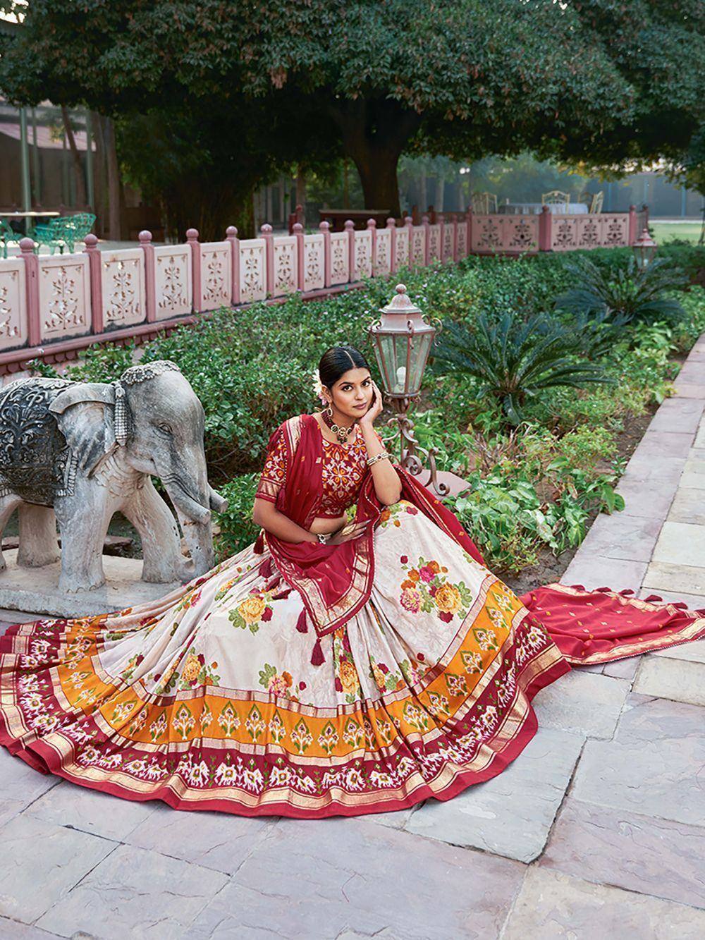 Woman in red and cream floral lehenga choli with elephant statue in garden