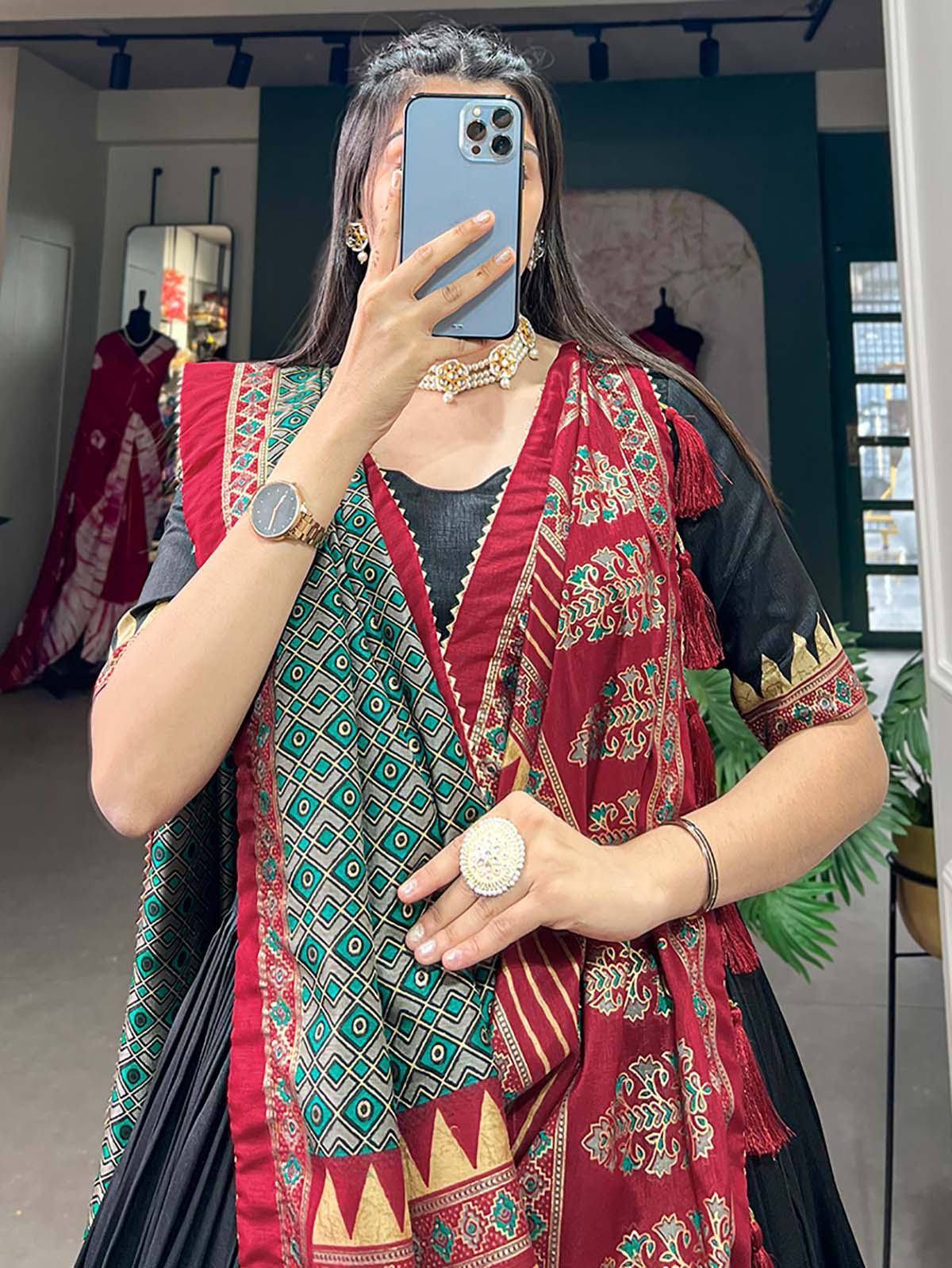 Woman wearing black and red printed ethnic kurta with dupatta, gold jewelry, taking mirror selfie in boutique