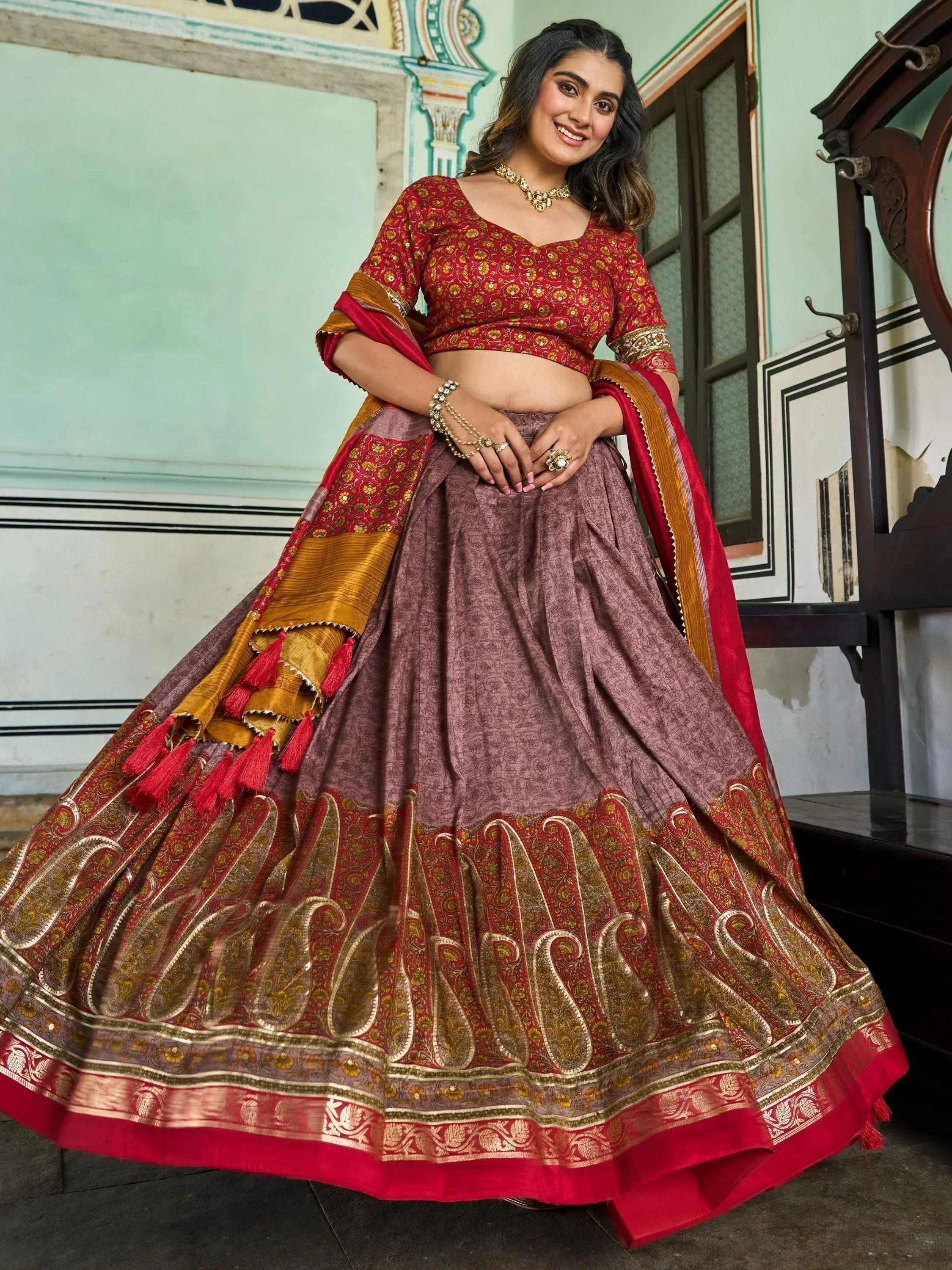 Woman in red and maroon designer lehenga choli with gold embroidery and tassels, ethnic Indian wear