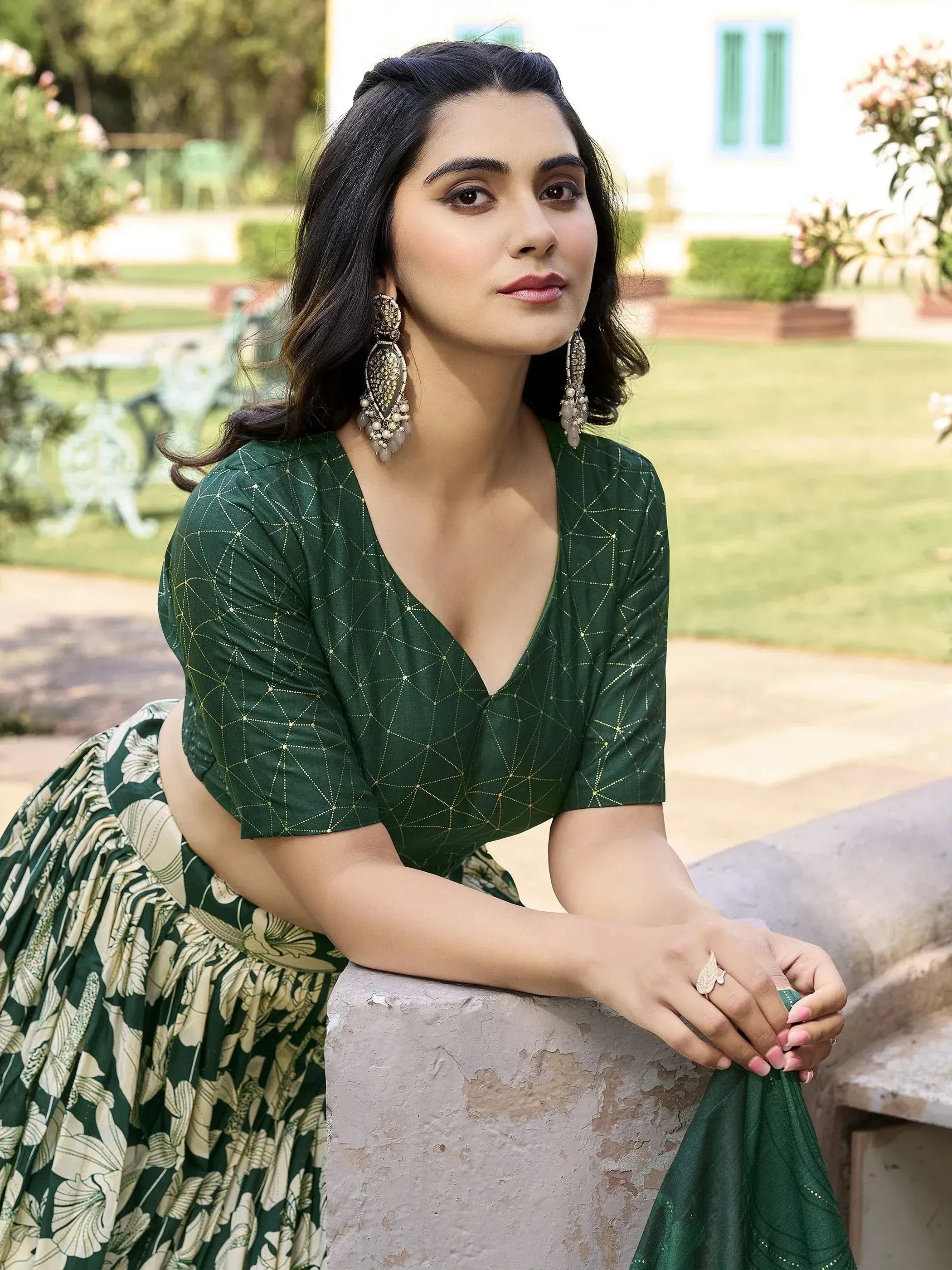 Woman in green embroidered lehenga choli with floral skirt, gold detailing, and statement earrings