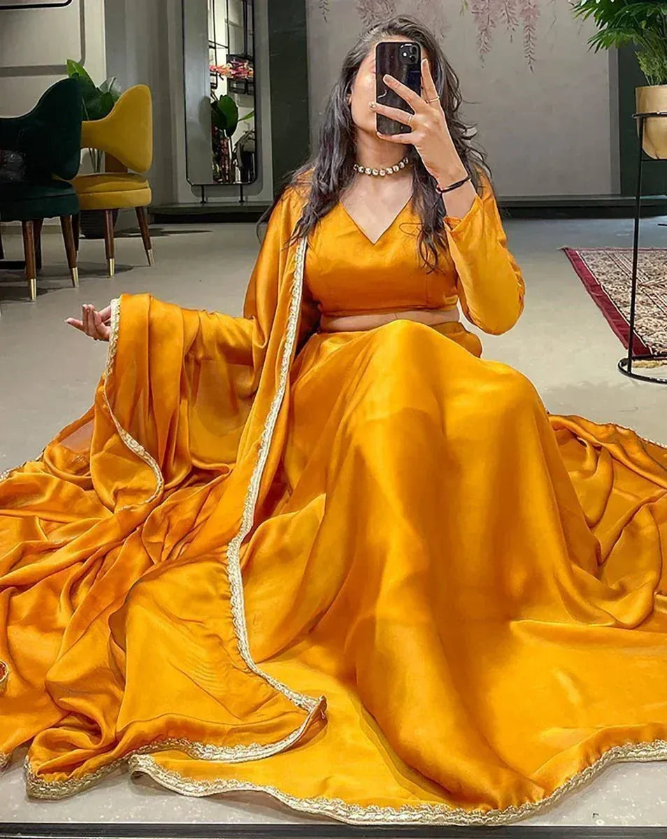 Woman in vibrant mustard yellow lehenga choli with gold trim, taking mirror selfie in modern studio