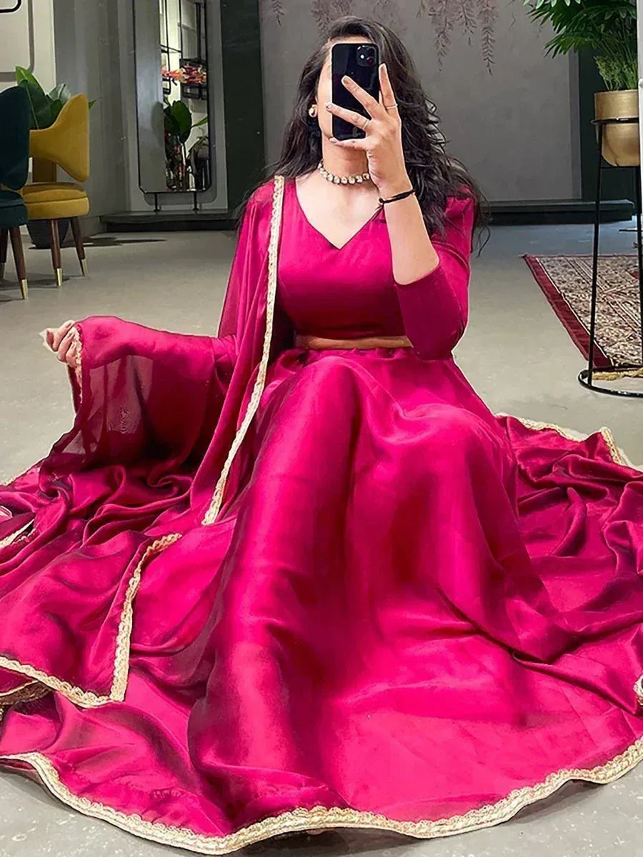Woman in vibrant pink designer lehenga choli with gold trim, taking mirror selfie in modern room