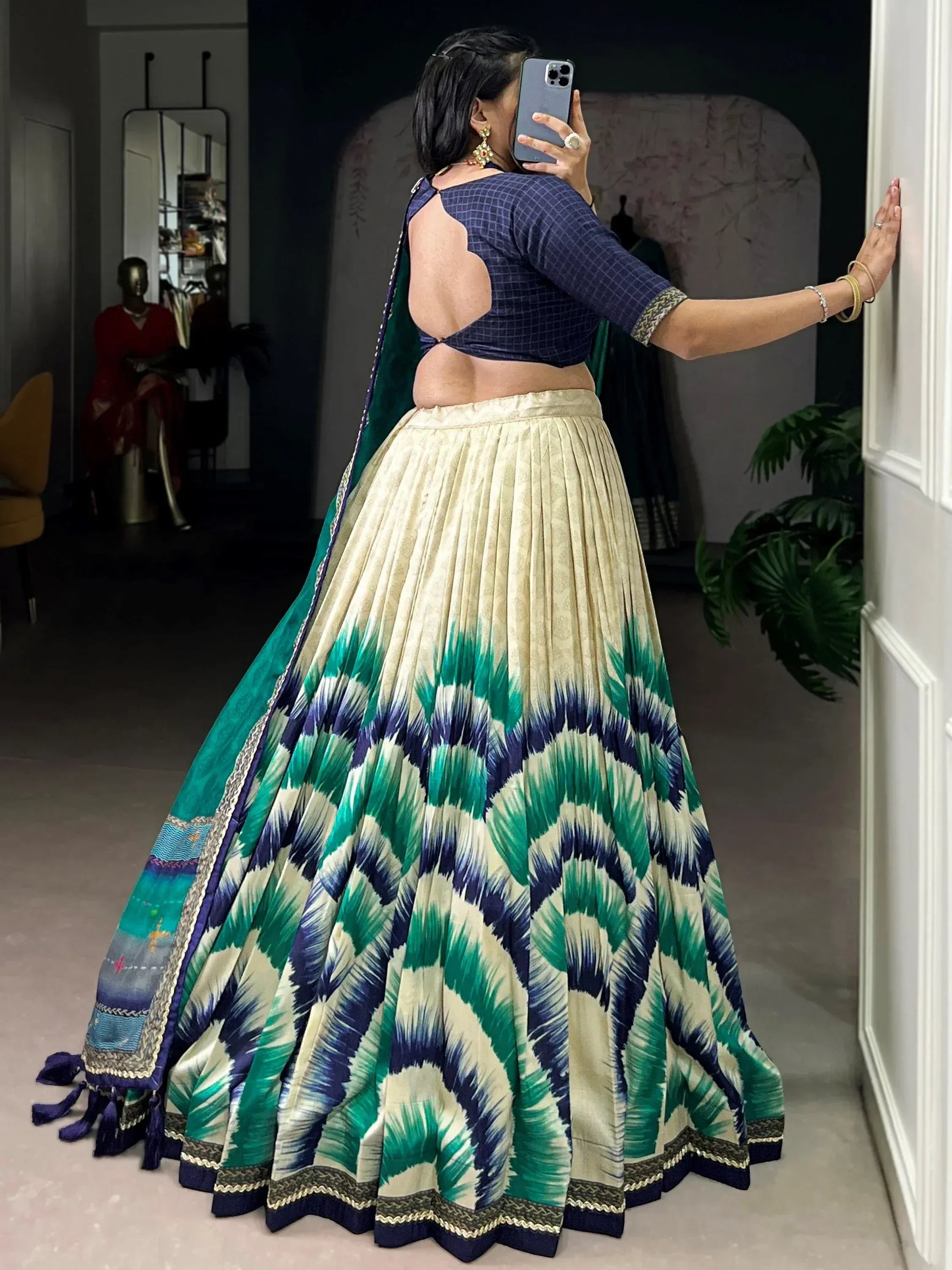 Woman in elegant lehenga choli with green and blue ikat print, backless blouse, and pleated skirt, perfect for ethnic occasions.