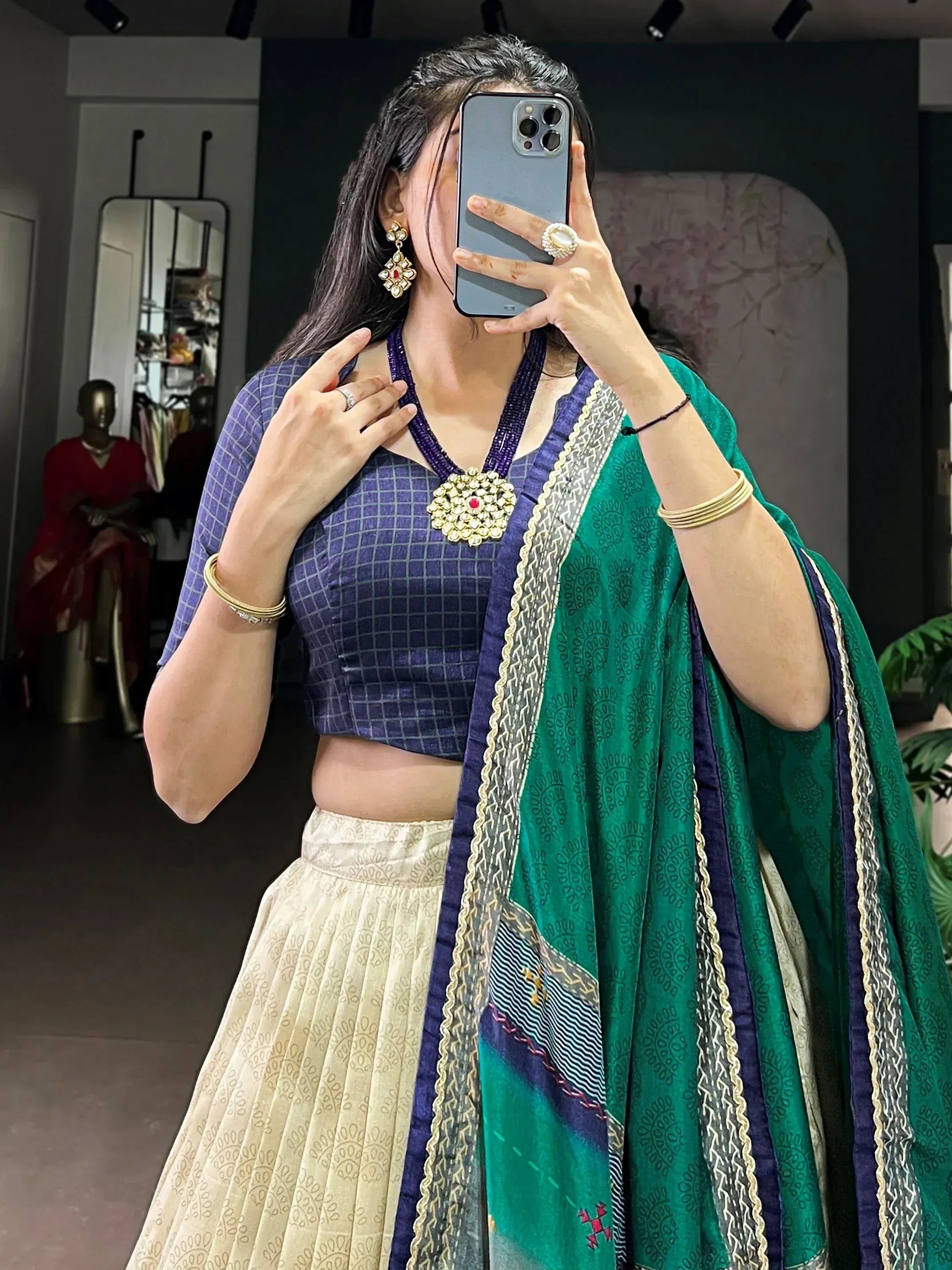 Woman in purple crop top and cream lehenga with green dupatta, accessorized with gold jewelry.