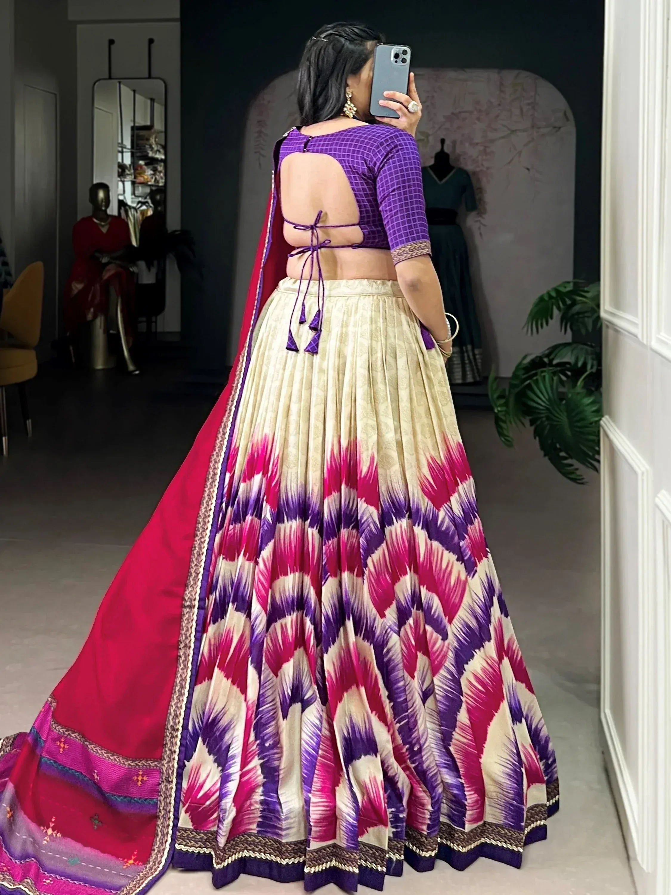 Purple backless blouse with tie-up detail, cream lehenga with pink and purple ikat print, and red dupatta.